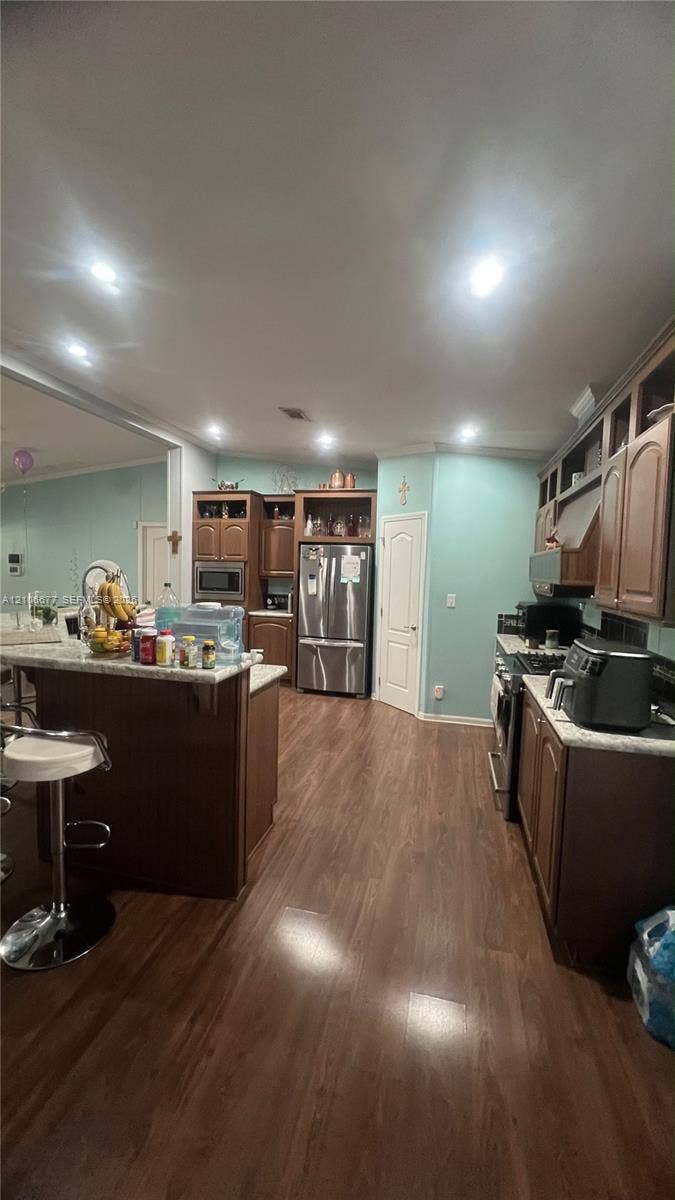 Kitchen featuring wood-finish cabinetry, stone-style countertops, stainless steel appliances, and wood-finish flooring