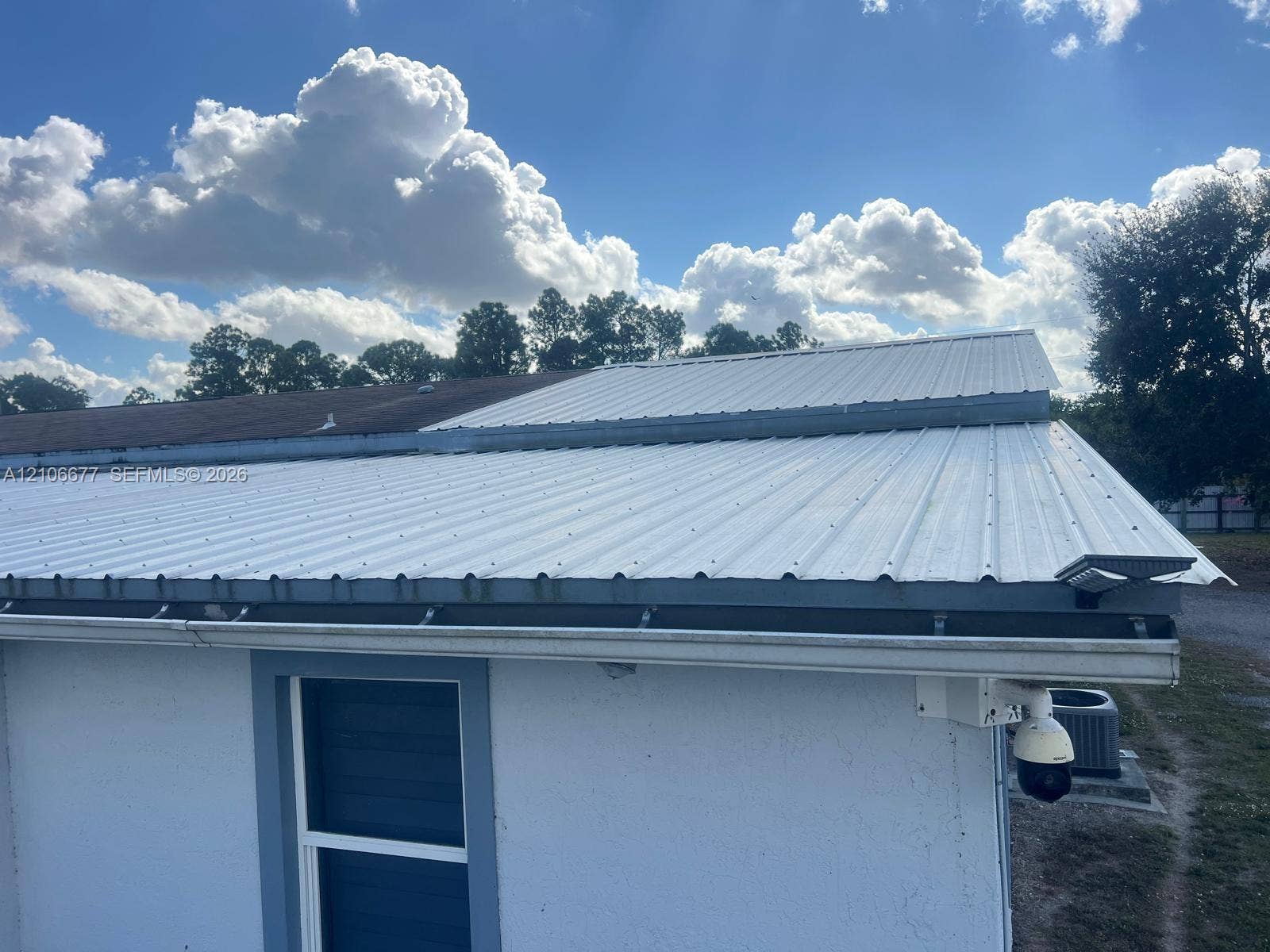Standing seam metal roofing, white exterior finish, integrated gutter system, and security camera fixture