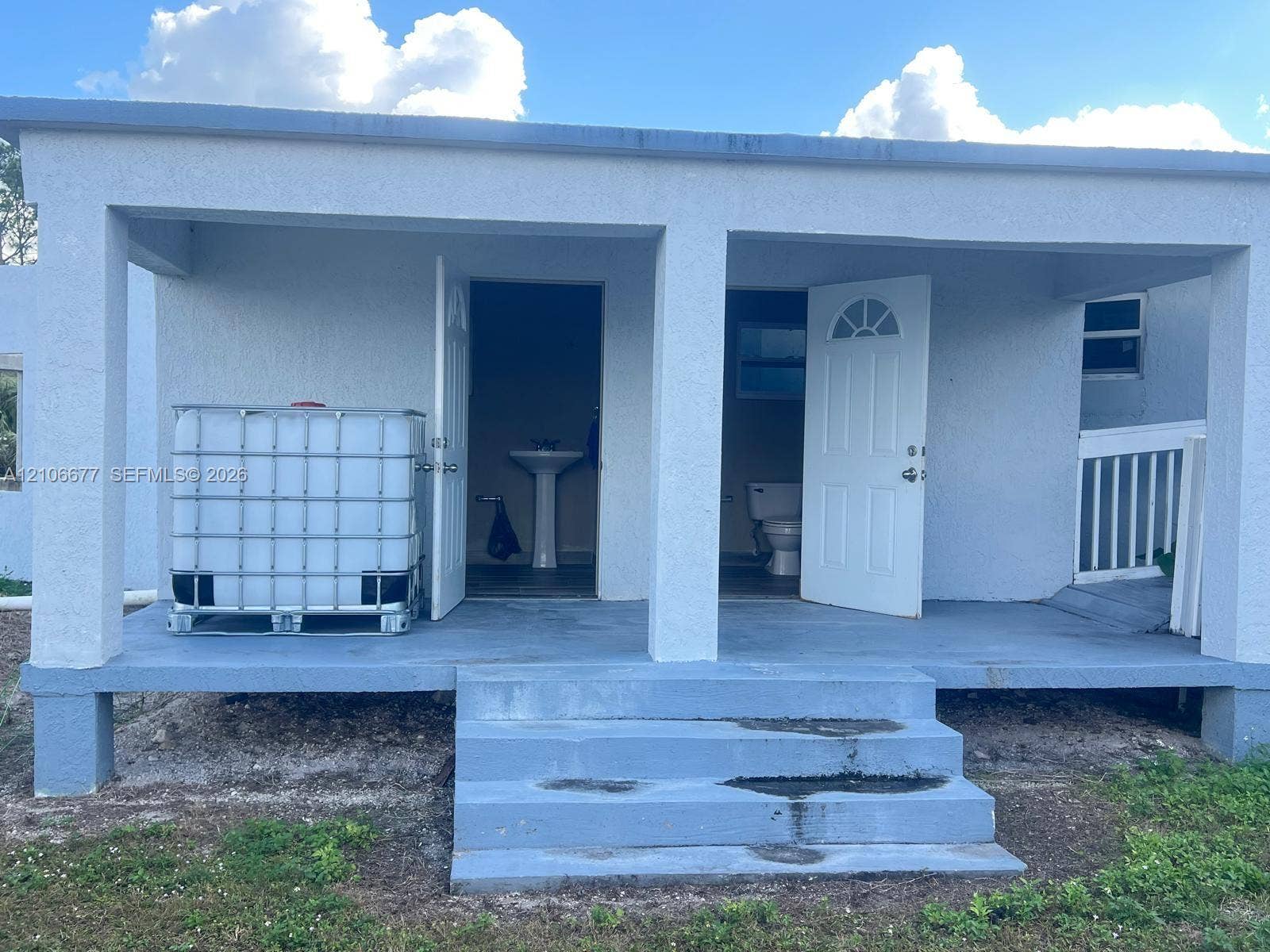 Covered porch featuring painted concrete flooring, masonry support pillars, concrete steps, and two entry points with arched-detail doors