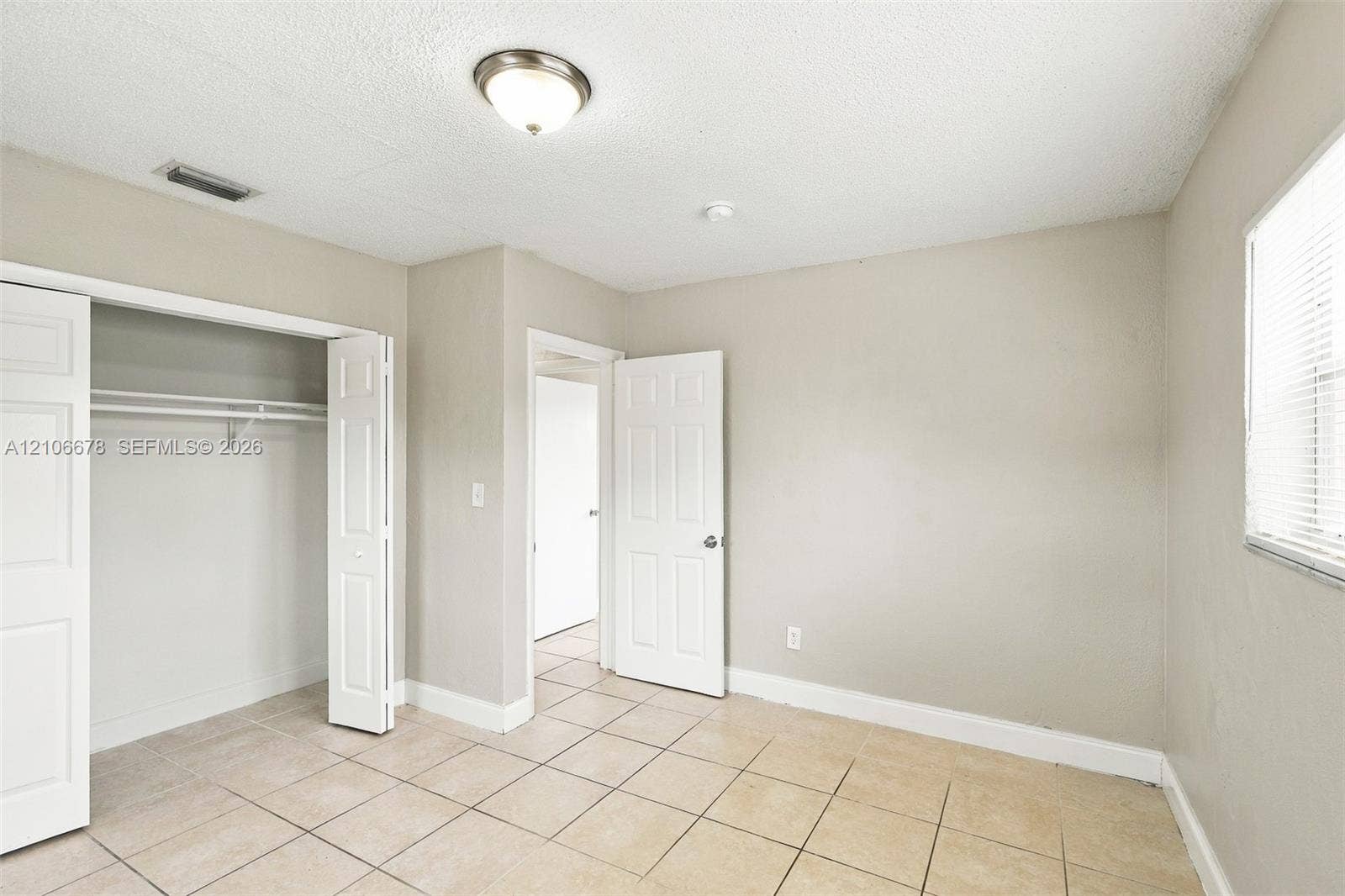 Neutral-toned walls, tile flooring, built-in closet with double doors, and ceiling-mounted flush light fixture