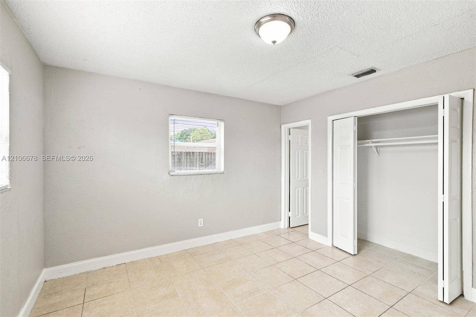 Neutral-toned room with tile flooring, dual-pane window, flush-mount ceiling light, and built-in closet with double-hinged doors