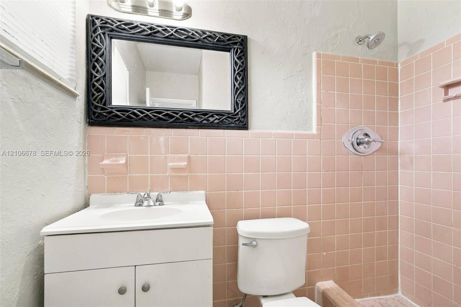 Bathroom featuring pink ceramic tile wall surfacing, a white vanity with an integrated sink, a chrome single-handle shower faucet, and a wall-mounted light fixture