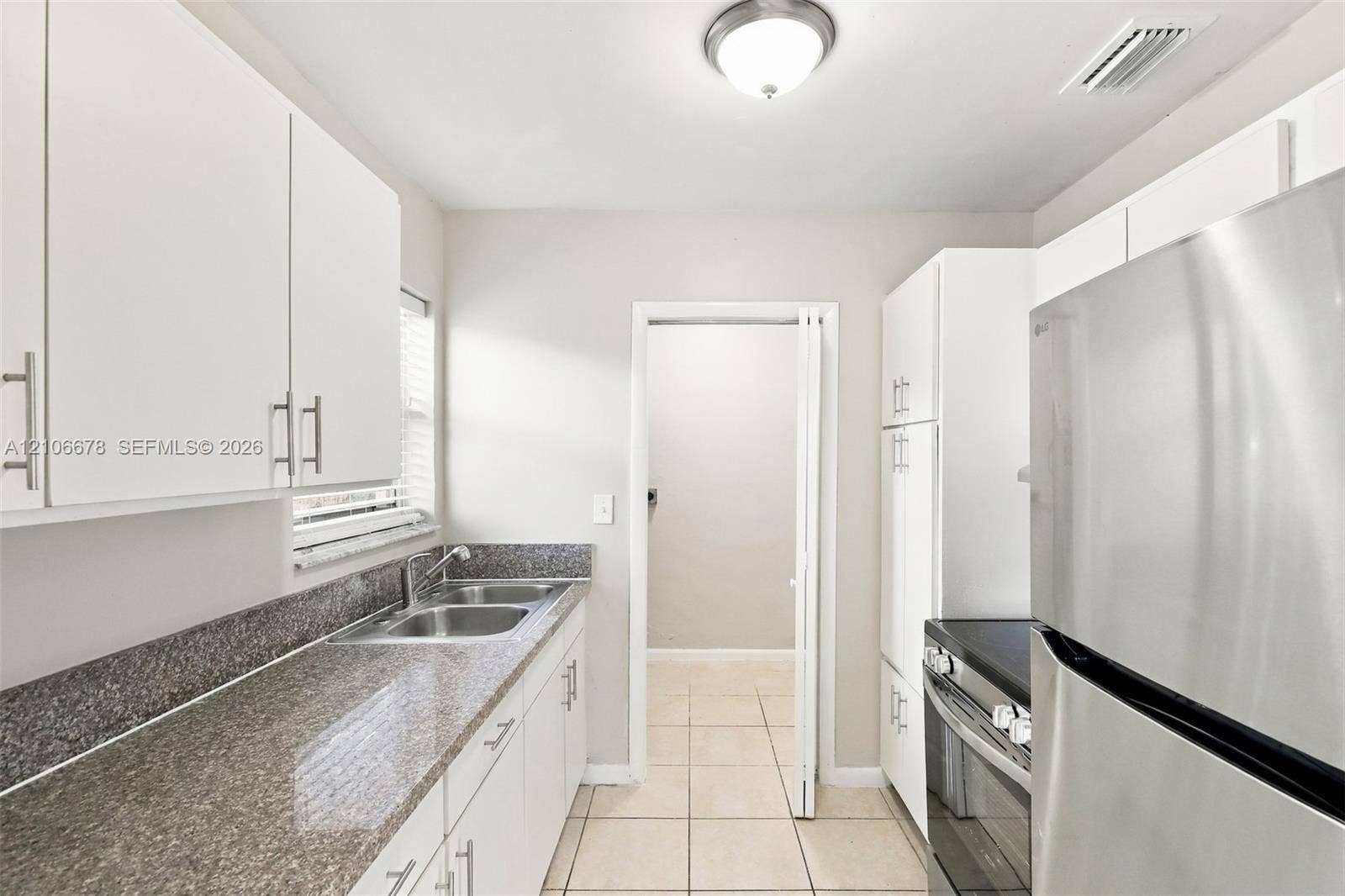 Kitchen featuring white cabinetry, stone-surface countertops, dual-basin stainless steel sink, stainless steel appliance, and tile flooring