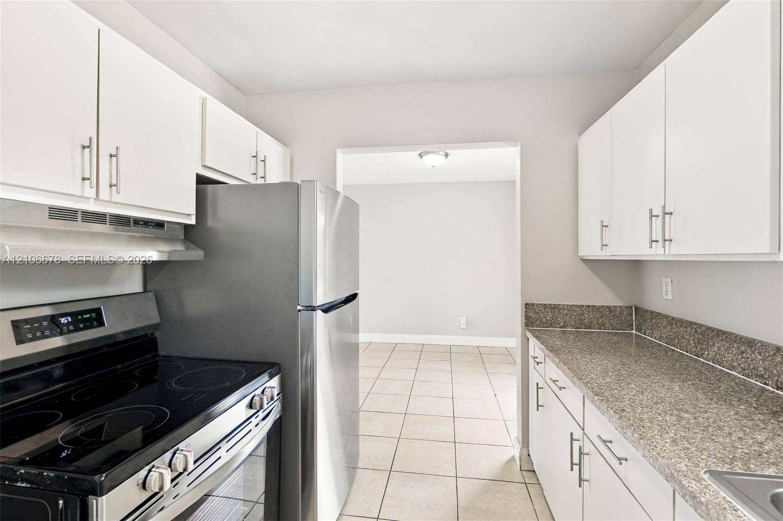 Kitchen featuring white cabinetry with brushed metal hardware, speckled stone-finish countertops, stainless steel appliances, and neutral tile flooring