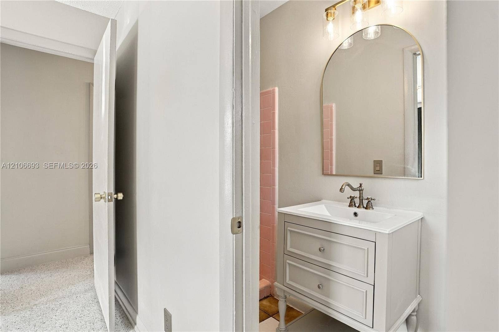1459 42nd Street, West Palm Beach, FL 33407 Bathroom featuring a vanity with two drawers and an integrated countertop, arched wall mirror, three-light vanity fixture, and pink tiled wall accents