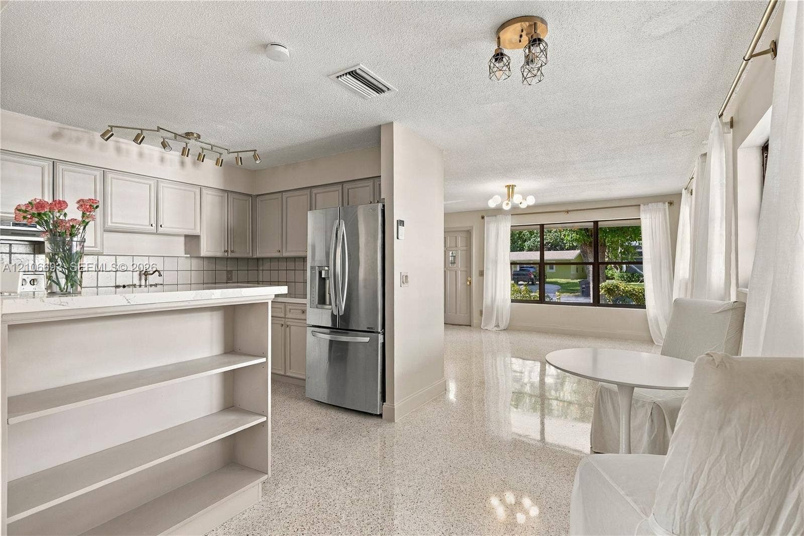 1459 42nd Street, West Palm Beach, FL 33407 Kitchen featuring white cabinetry, stainless steel refrigerator, tile backsplash, multi-bulb track lighting, and terrazzo flooring