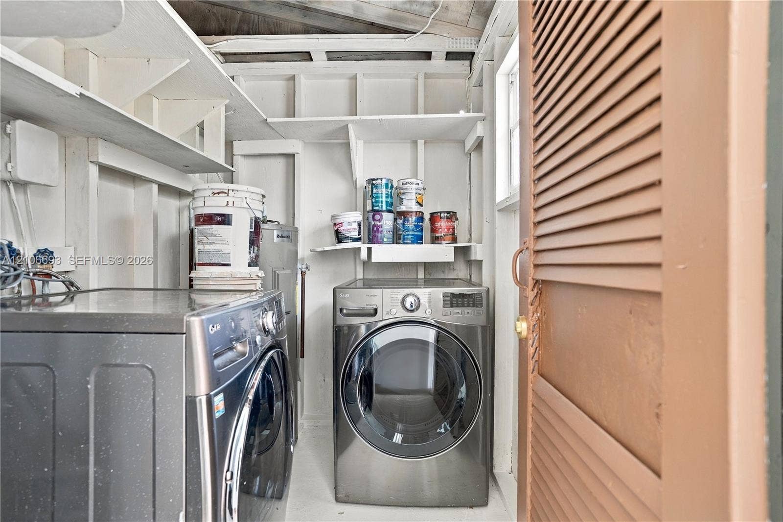 1459 42nd Street, West Palm Beach, FL 33407 Laundry space featuring built-in open shelving, louvered door, and exposed structural framing