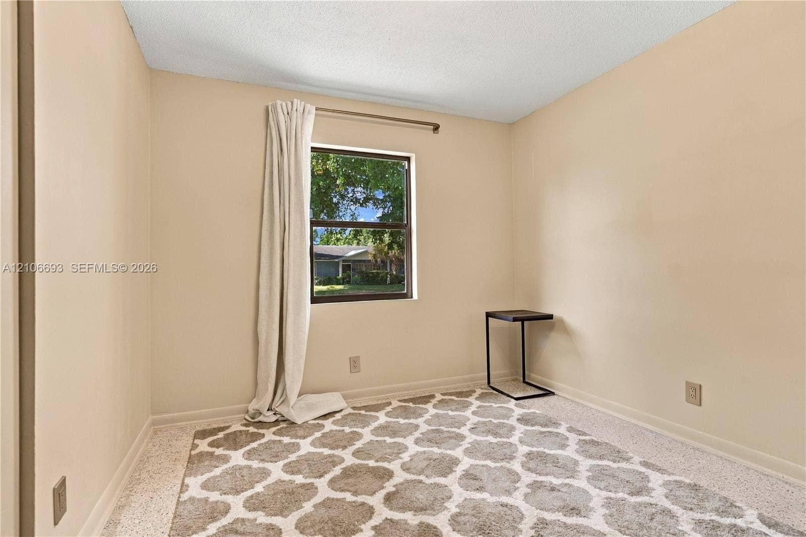 1459 42nd Street, West Palm Beach, FL 33407 Neutral-toned room featuring a single-pane window with dark trim, textured ceiling, and terrazzo flooring