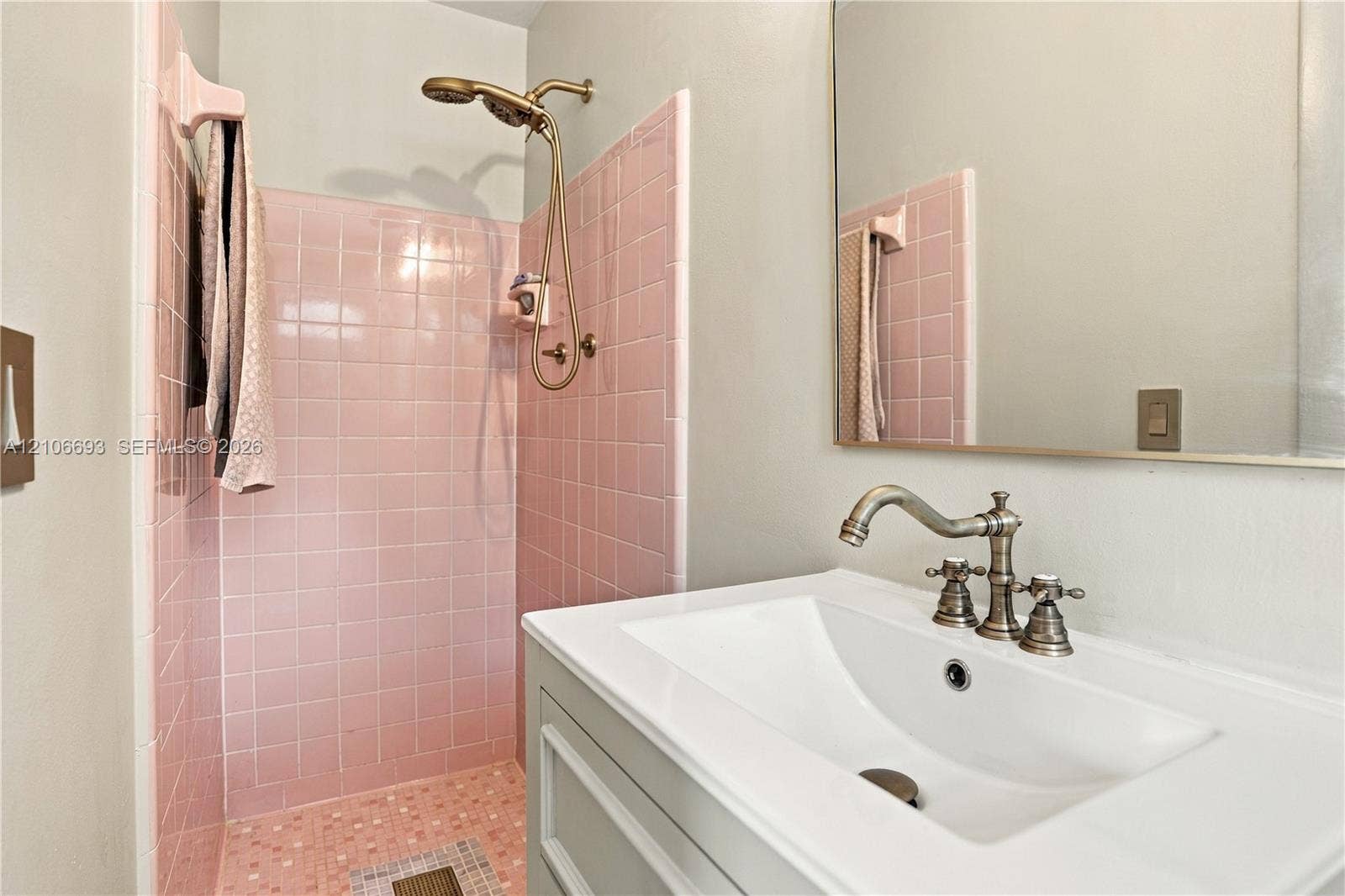 1459 42nd Street, West Palm Beach, FL 33407 Bathroom featuring square pink tile shower surround, brass-finish handheld shower fixture, rectangular white undermount sink, brass-finish widespread faucet, and large frameless mirror