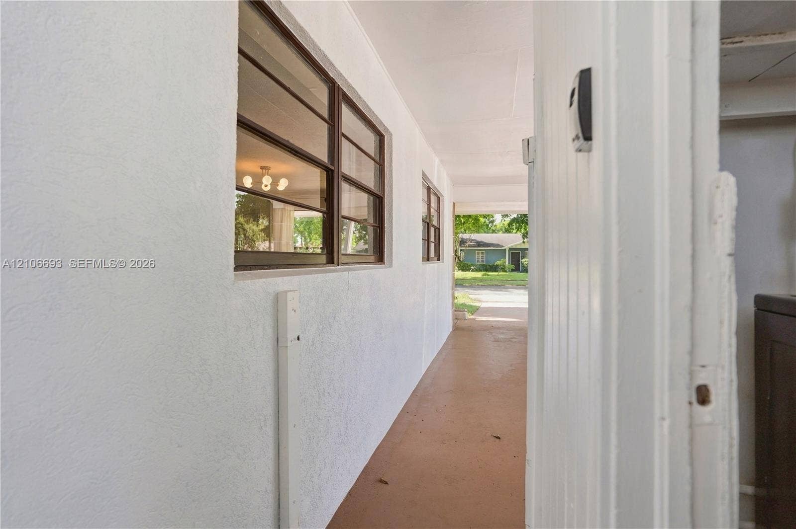 1459 42nd Street, West Palm Beach, FL 33407 Covered exterior walkway featuring a smooth stucco finish, horizontal sliding windows with dark metal frames, and solid concrete flooring