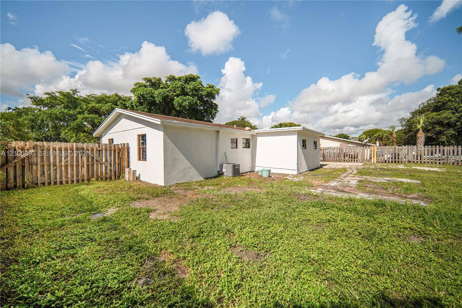 1459 42nd Street, West Palm Beach, FL 33407 Exterior rear elevation featuring a stucco finish, gable roofline, wood privacy fencing, and an expansive lawn