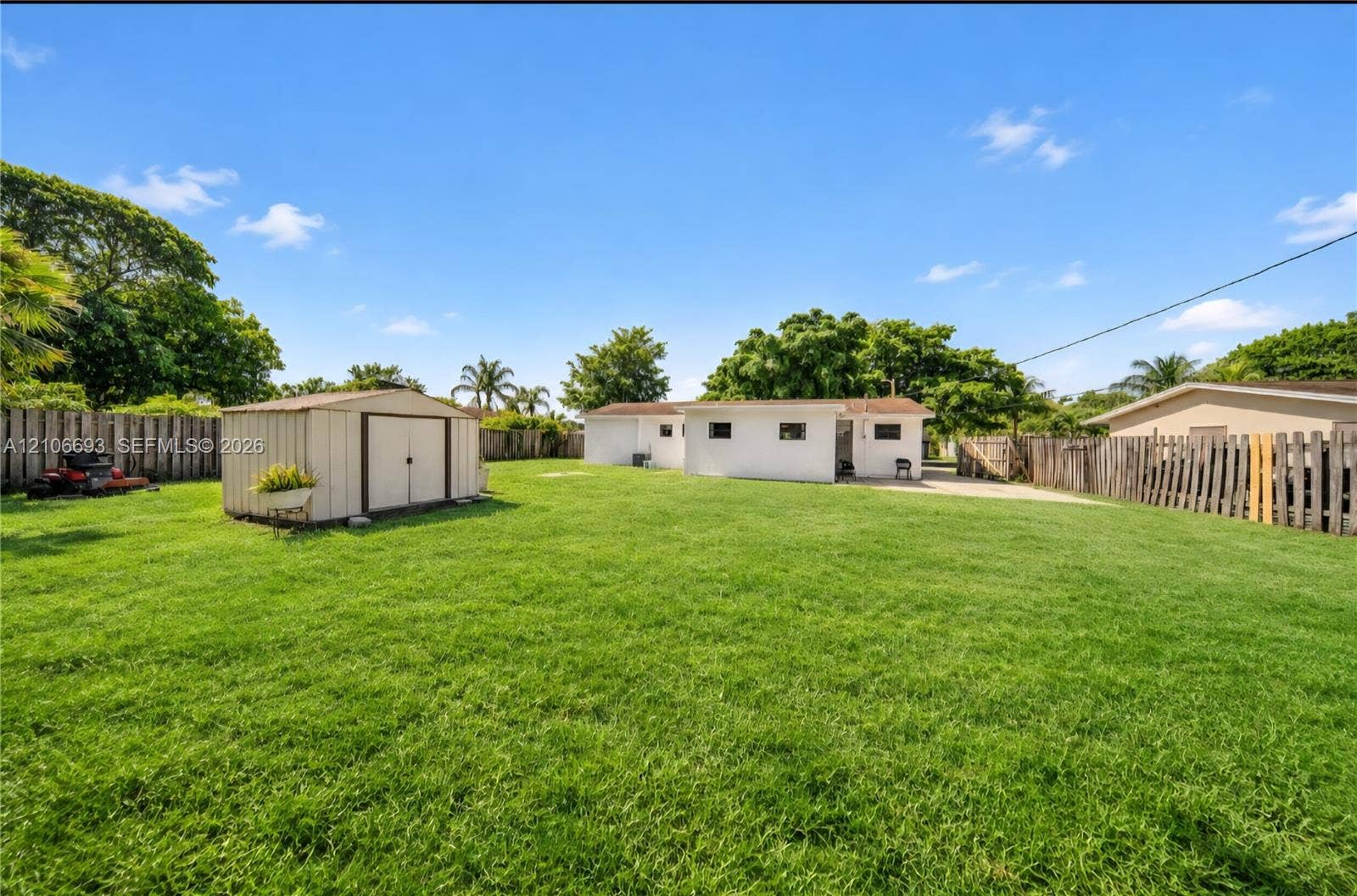1459 42nd Street, West Palm Beach, FL 33407 Expansive backyard featuring a large grass lawn, perimeter wood fencing, and a detached storage shed