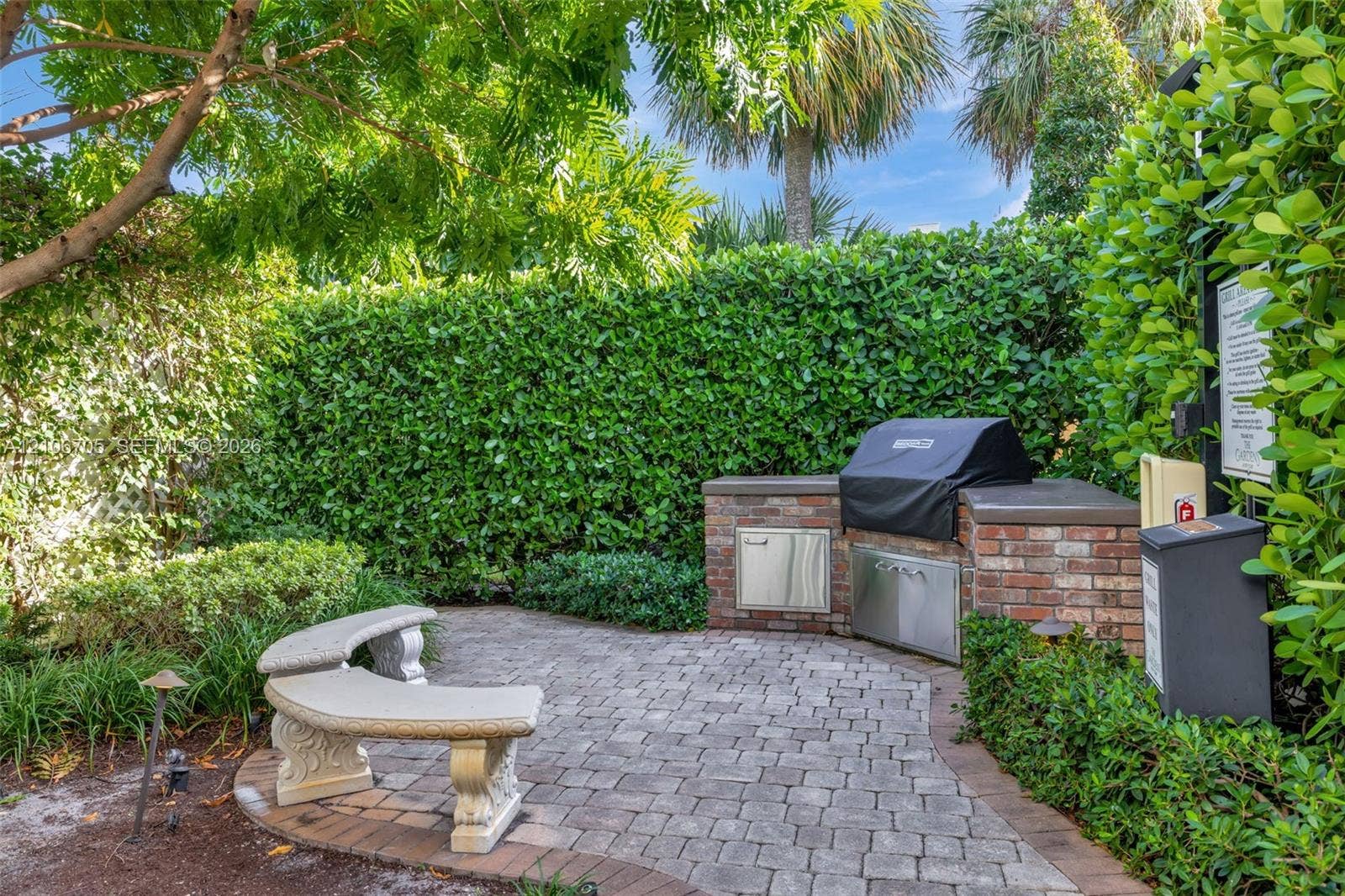 Outdoor kitchen featuring a brick-base grill station with stainless steel access doors, paver patio, and curved stone bench