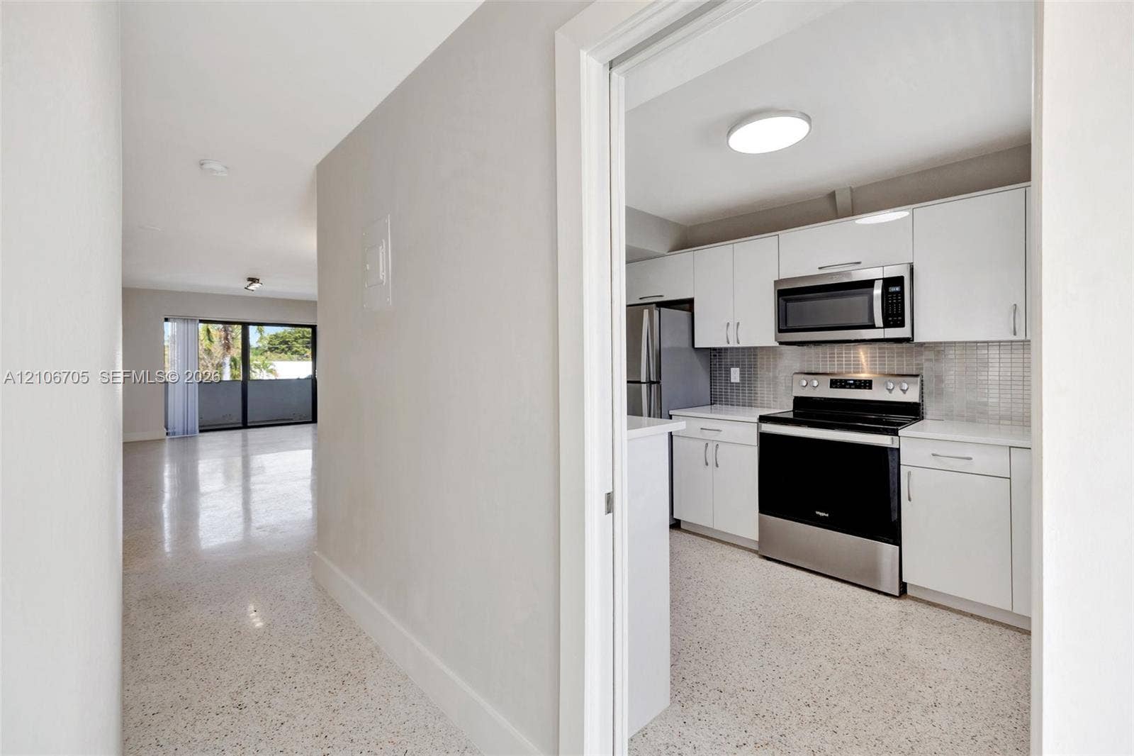 Kitchen featuring white shaker-style cabinetry, stainless steel appliances, and a tiled backsplash, finished with terrazzo flooring throughout