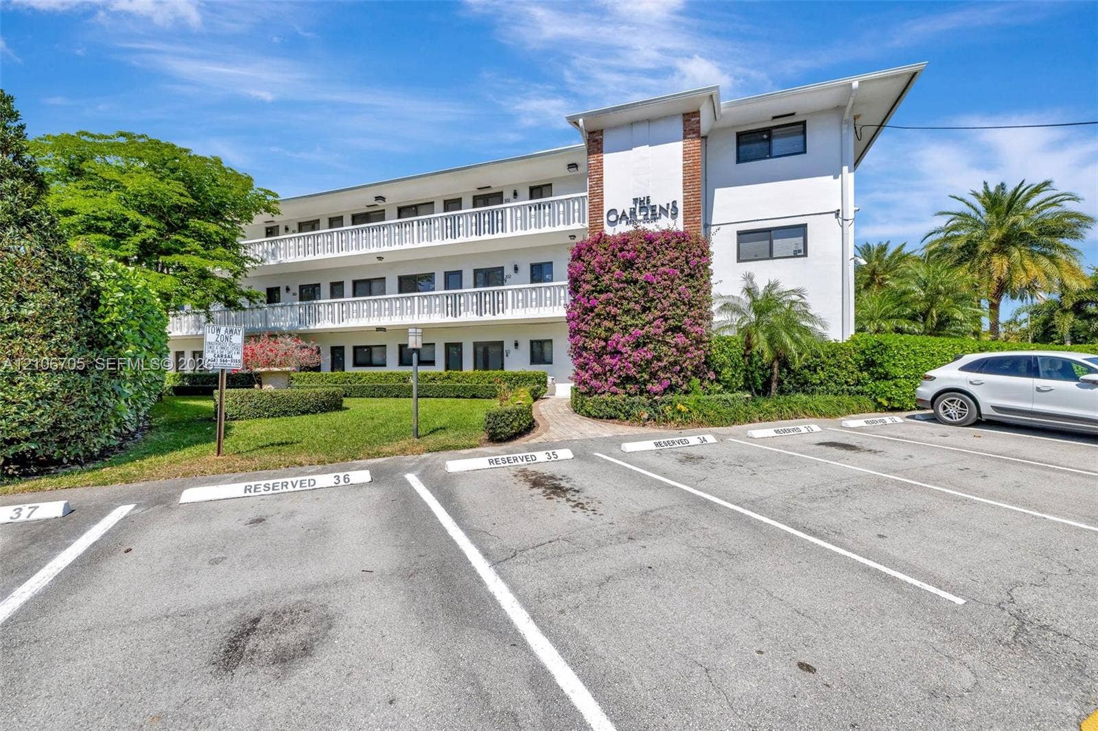 Multi-story exterior featuring white stucco cladding, brick accents, white railed balconies, and landscaped grounds with mature shrubbery