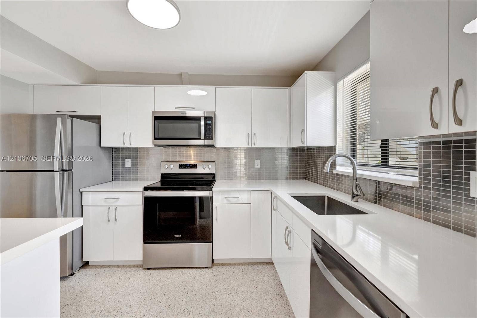 Kitchen featuring high-gloss white cabinetry, white stone countertops, stainless steel appliances, a mosaic tile backsplash, and a stainless steel undermount sink