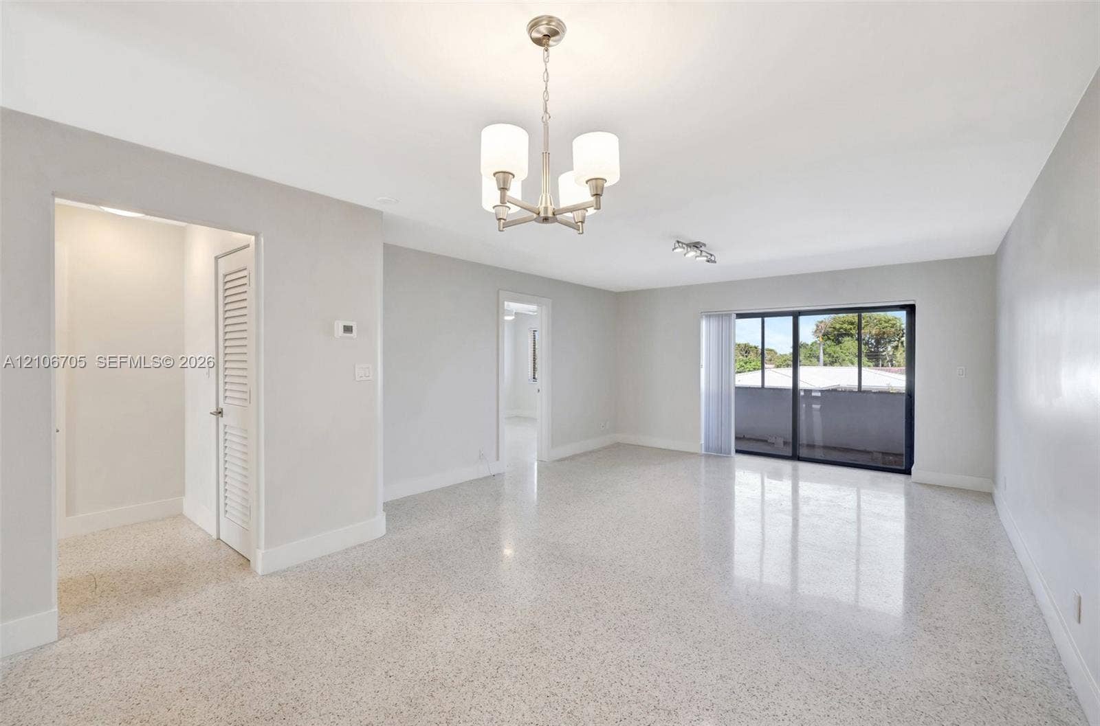 Open-concept interior featuring polished terrazzo flooring, a multi-arm chandelier with glass shades, and sliding glass doors with dark frames