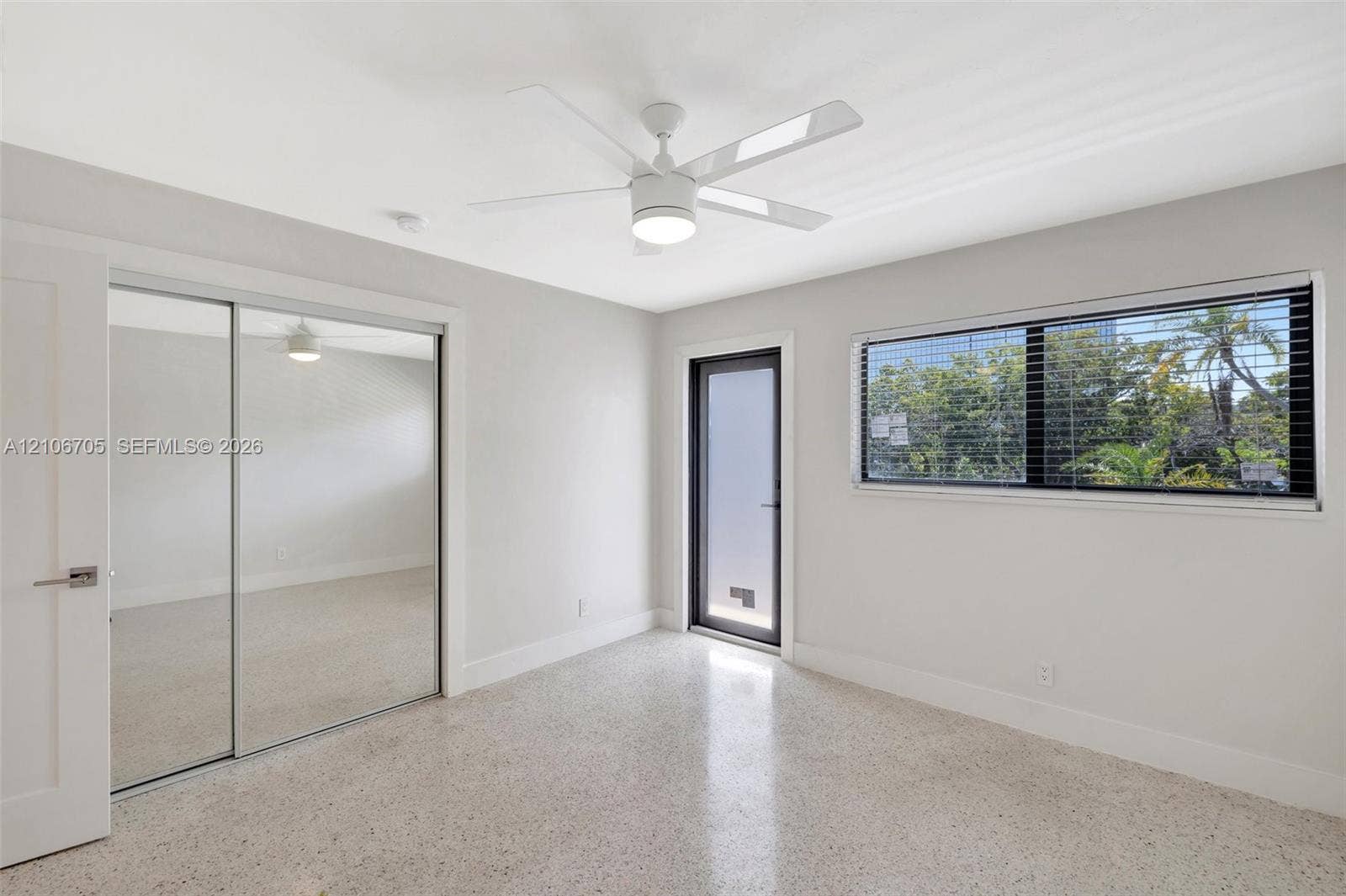 Terrazzo flooring, white ceiling fan with integrated lighting, dual-panel mirrored sliding closet doors, and single-lite exterior glass door
