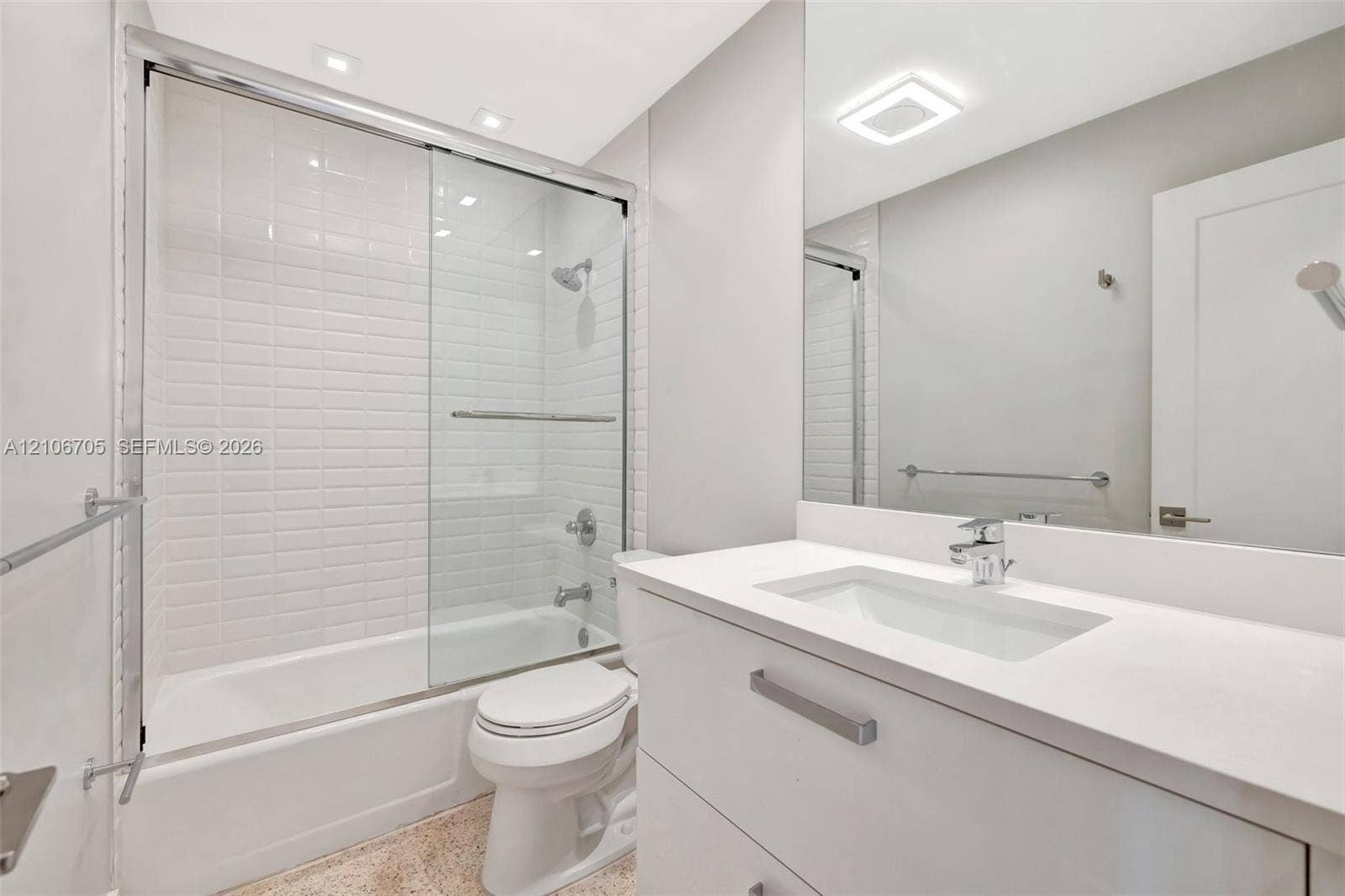 Bathroom featuring a white vanity with a composite countertop and integrated sink, a glass-enclosed shower with subway tile surround, recessed lighting, and a full-width vanity mirror