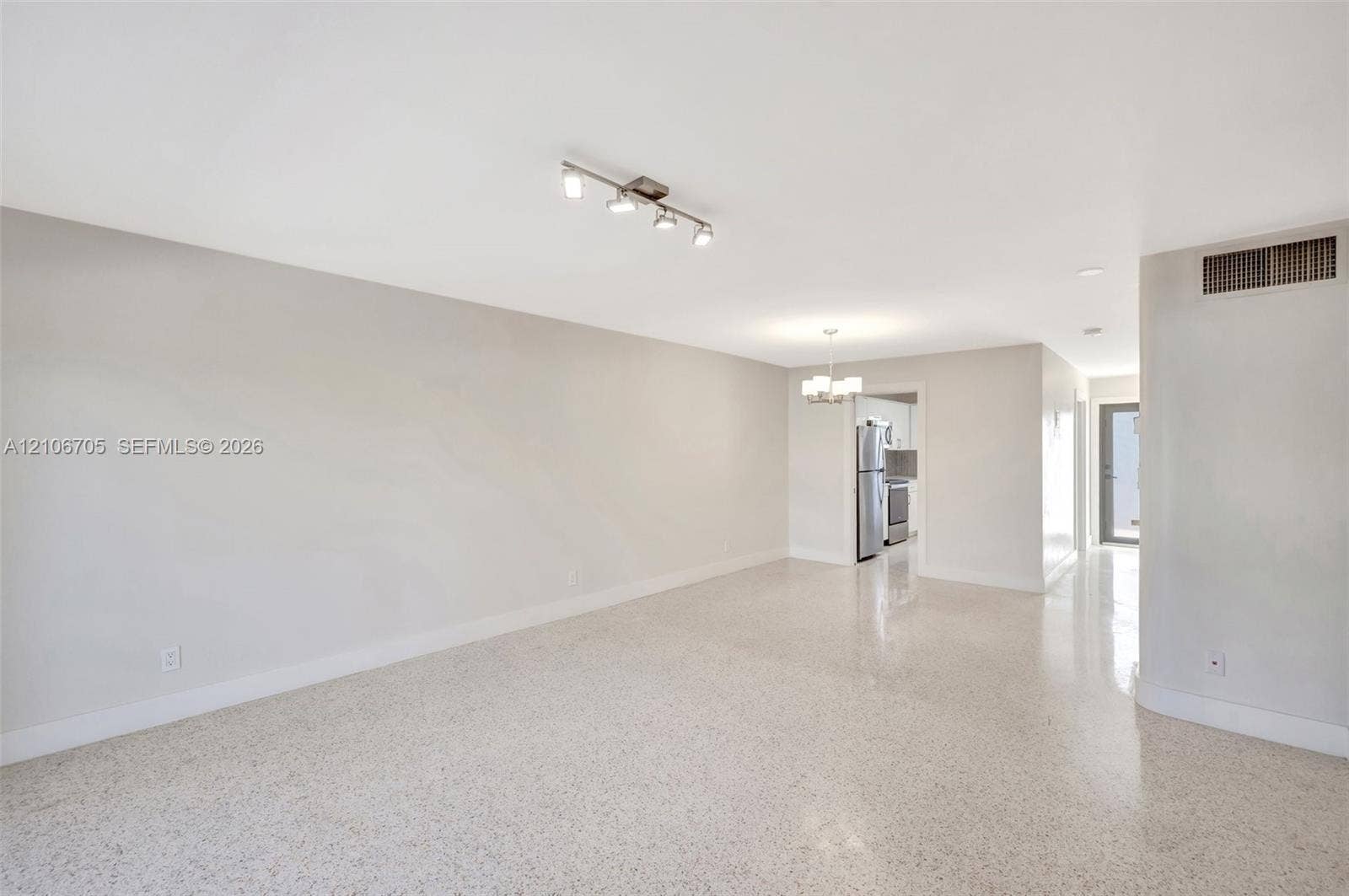 Open floor plan featuring neutral wall tones, polished terrazzo flooring, multi-light track lighting, and a pendant chandelier