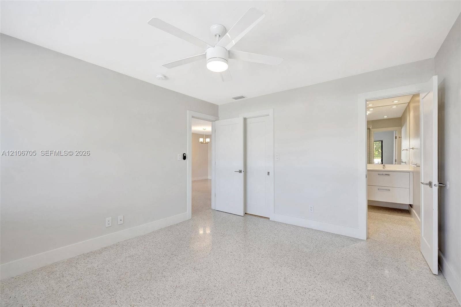 Interior space featuring light-toned stone flooring, a multi-blade ceiling fan with integrated lighting, solid-core interior doors, and a neutral color palette