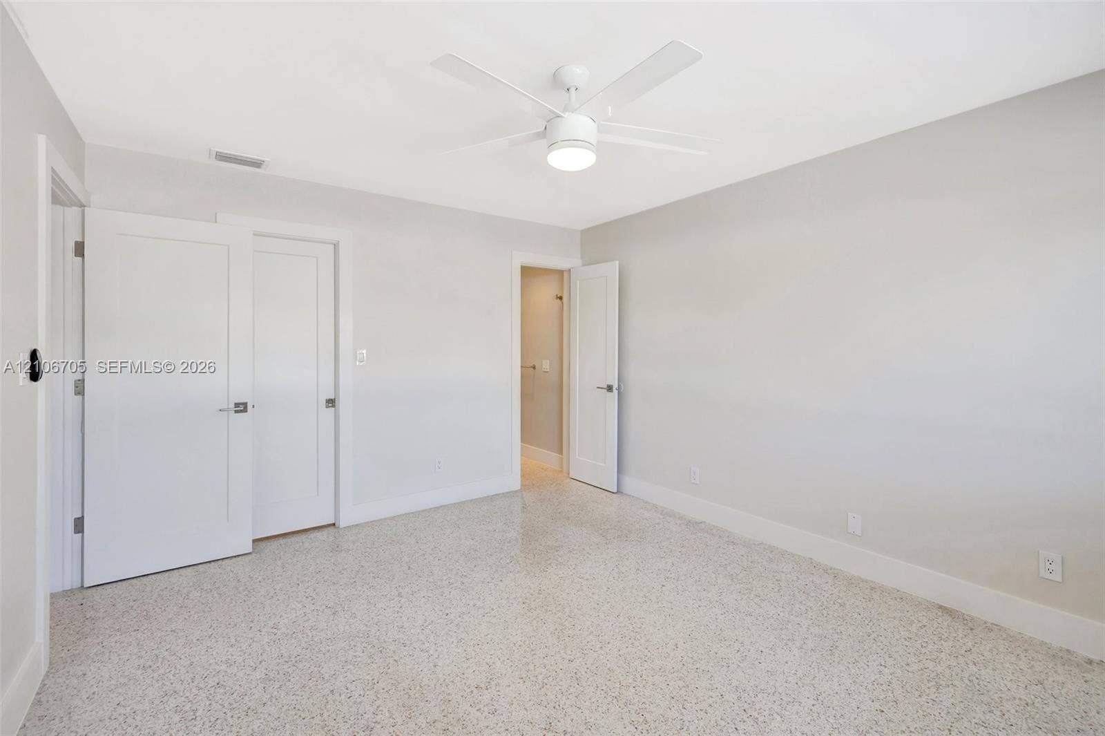 Interior space featuring neutral-toned walls, polished terrazzo flooring, a ceiling-mounted light fixture with fan, and three panel doors
