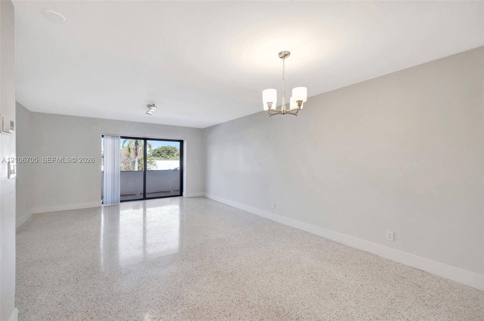 Open-concept interior featuring polished terrazzo flooring, neutral wall paint, a multi-arm chandelier with glass shades, and sliding glass doors