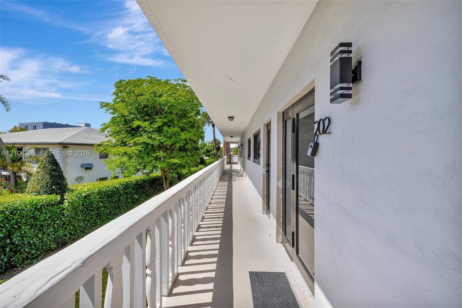 Exterior walkway featuring a white balustrade railing, smooth stucco walls, and dual-light modern wall sconces