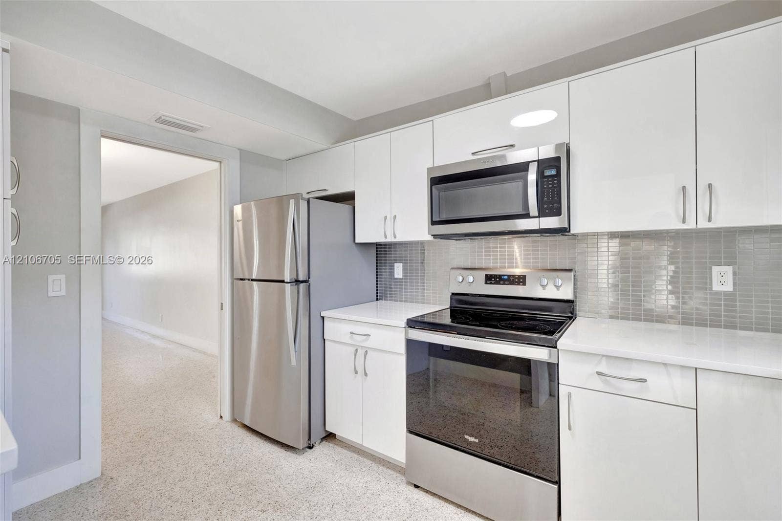 Kitchen featuring white cabinetry, solid-surface countertops, mosaic tile backsplash, and stainless steel appliances including a refrigerator, over-the-range microwave, and electric range