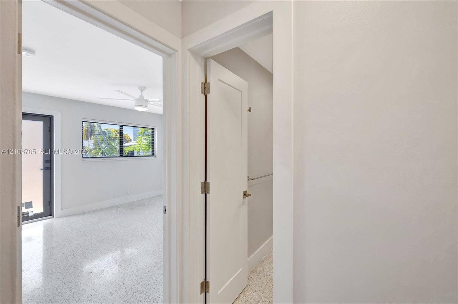Interior space featuring terrazzo flooring, shaker-style door with matte hardware, multi-pane window with dark trim, ceiling fan with integrated lighting, and a glass-paneled exterior door
