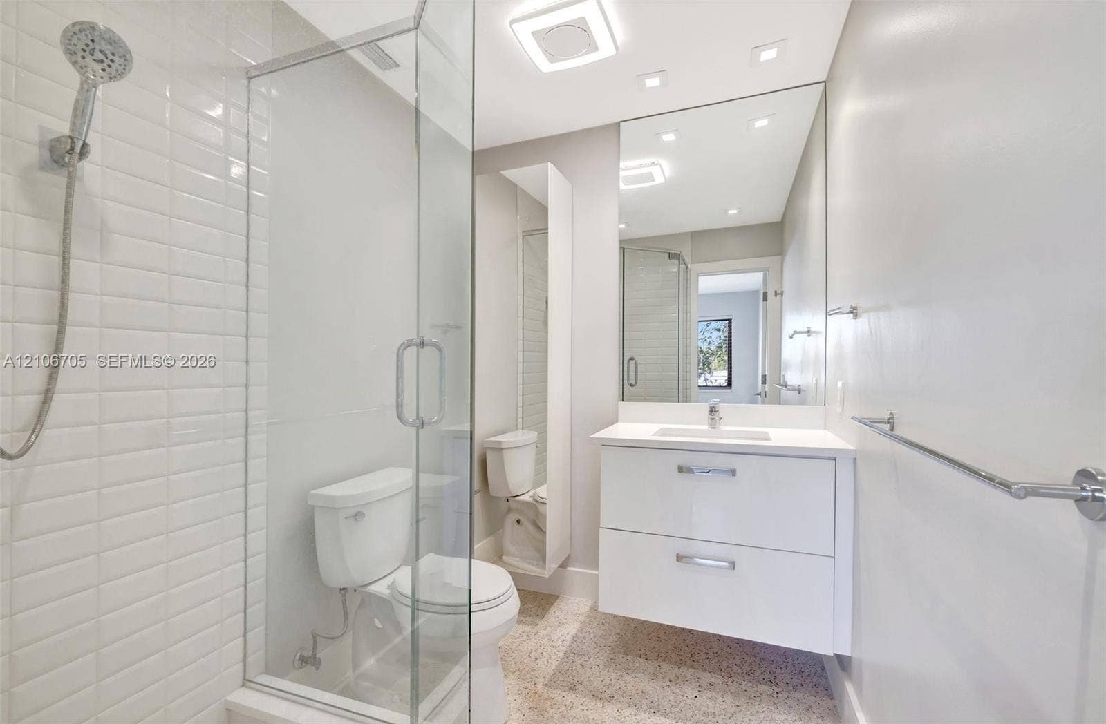 Bathroom featuring a white floating vanity with an integrated sink, a glass-enclosed shower with white subway tile surround, a large frameless mirror, and speckled flooring