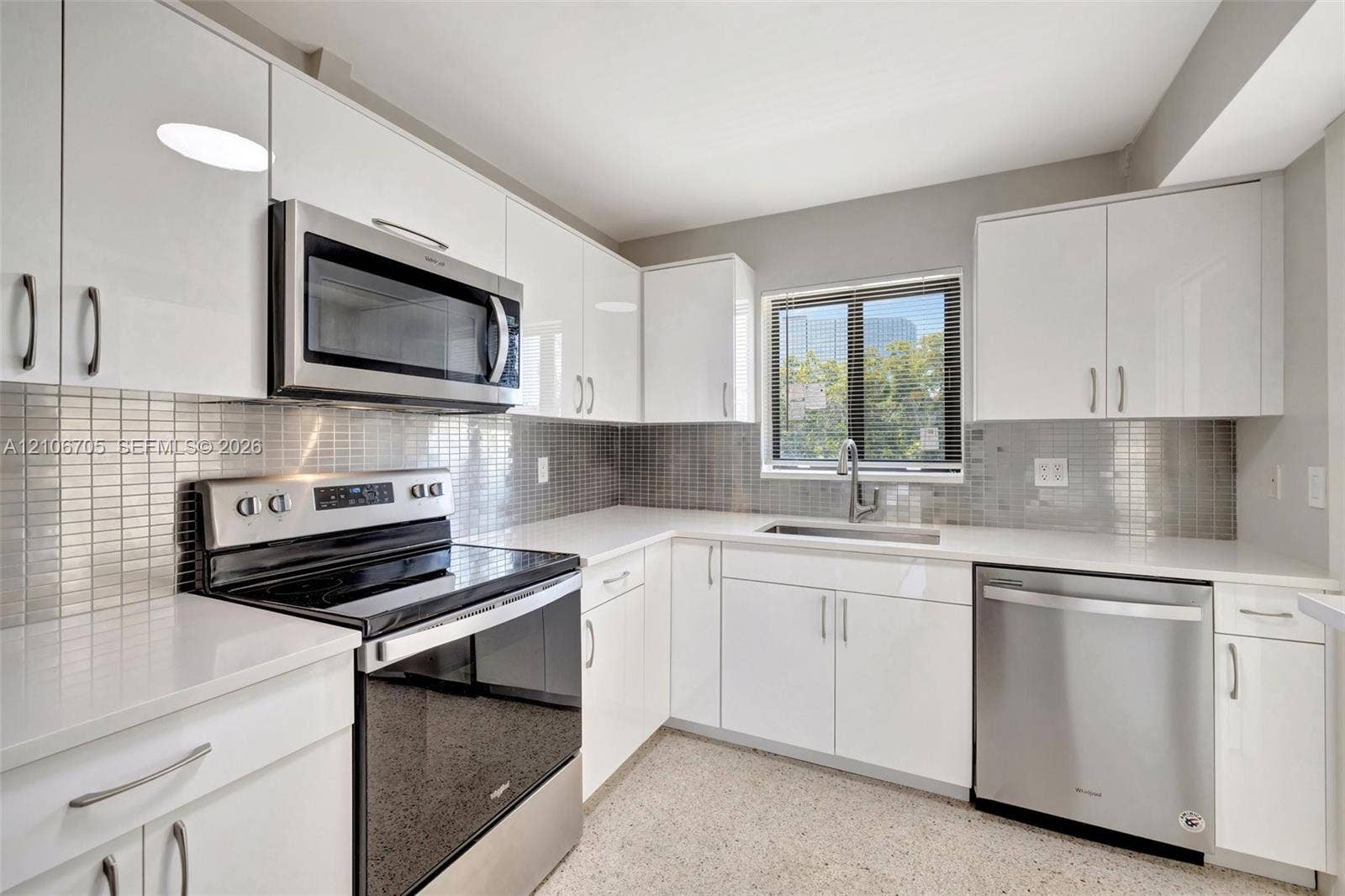Kitchen featuring high-gloss white cabinetry, white quartz countertops, stainless steel appliances, and a metallic mosaic tile backsplash