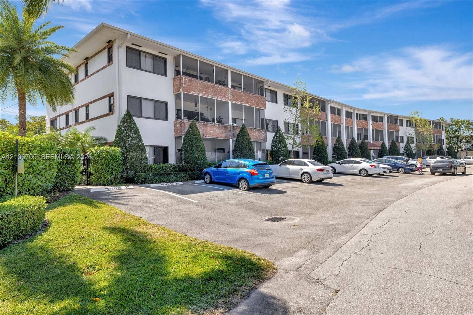 Multi-story building exterior featuring smooth stucco facade, brick-accented screening, and surface parking area