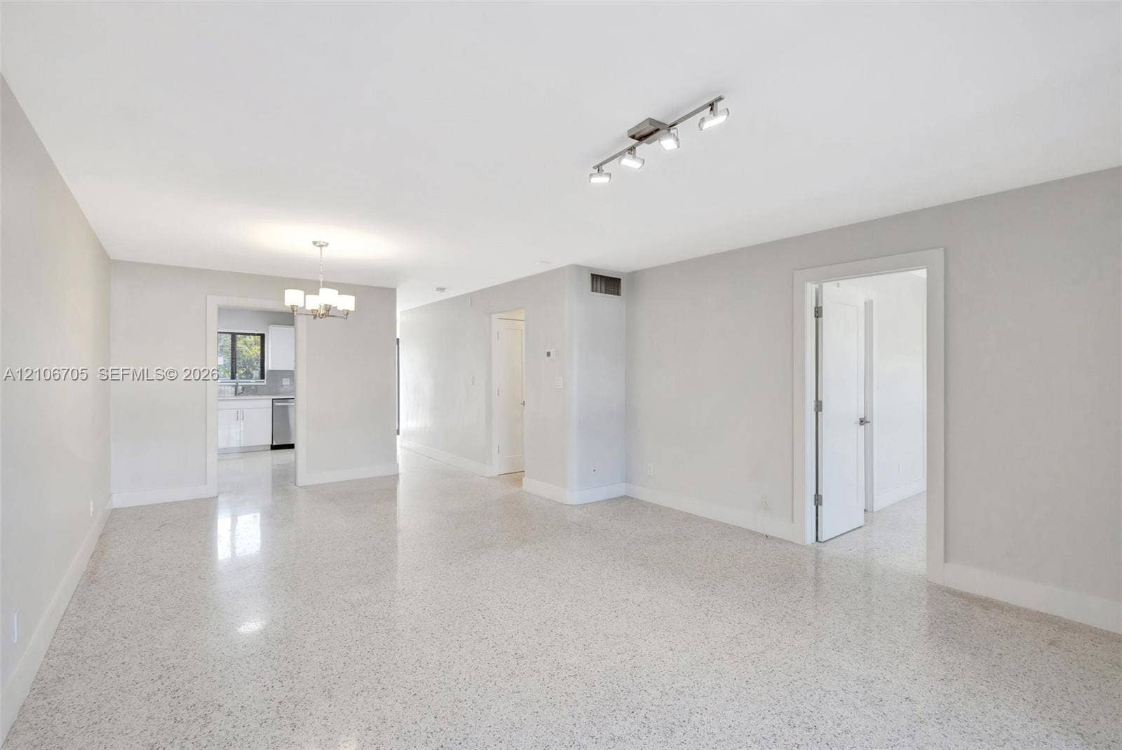Open-concept interior featuring light-toned stone-composite flooring, neutral wall finishes, multi-directional track lighting, and a multi-light decorative chandelier