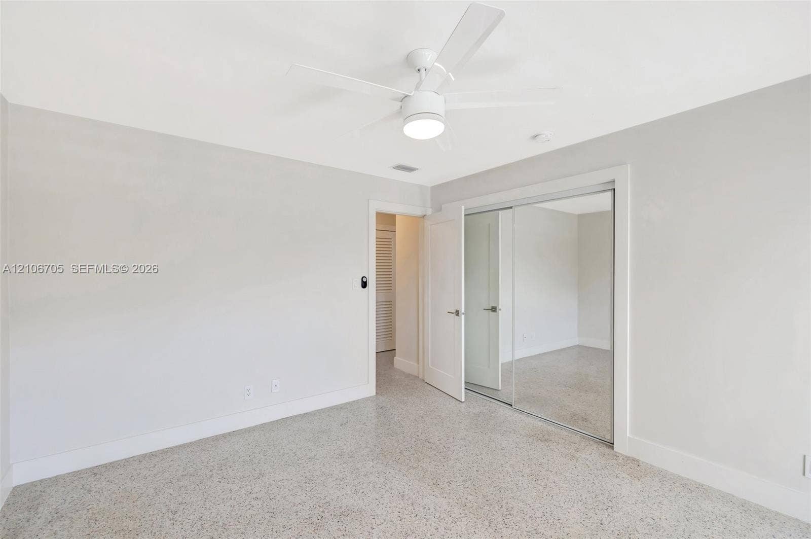 Neutral-toned interior featuring terrazzo flooring, a ceiling fan with integrated lighting, and a closet with mirrored sliding doors