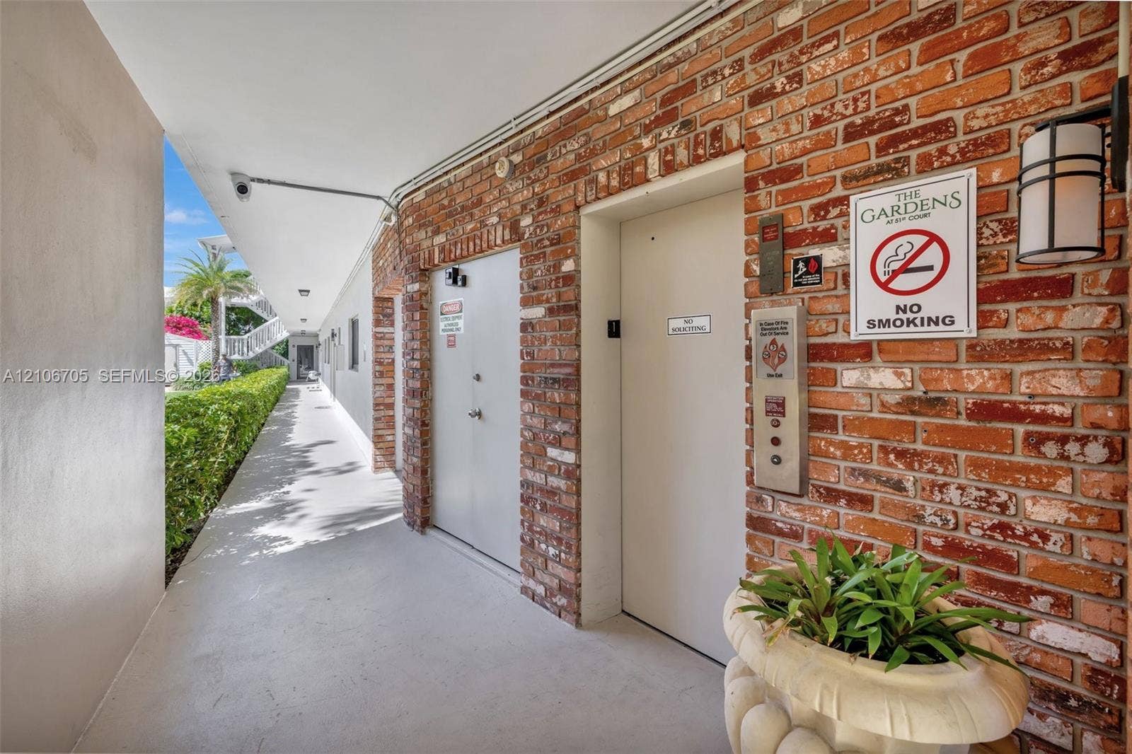 Exterior corridor featuring exposed brick masonry, concrete flooring, and metal-cased elevator access