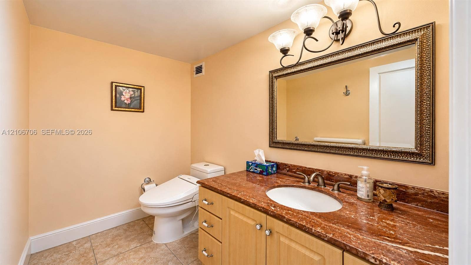 Bathroom featuring a vanity with a stone countertop, an integrated oval sink, a wall-mounted framed mirror, overhead three-light fixture, and tile flooring
