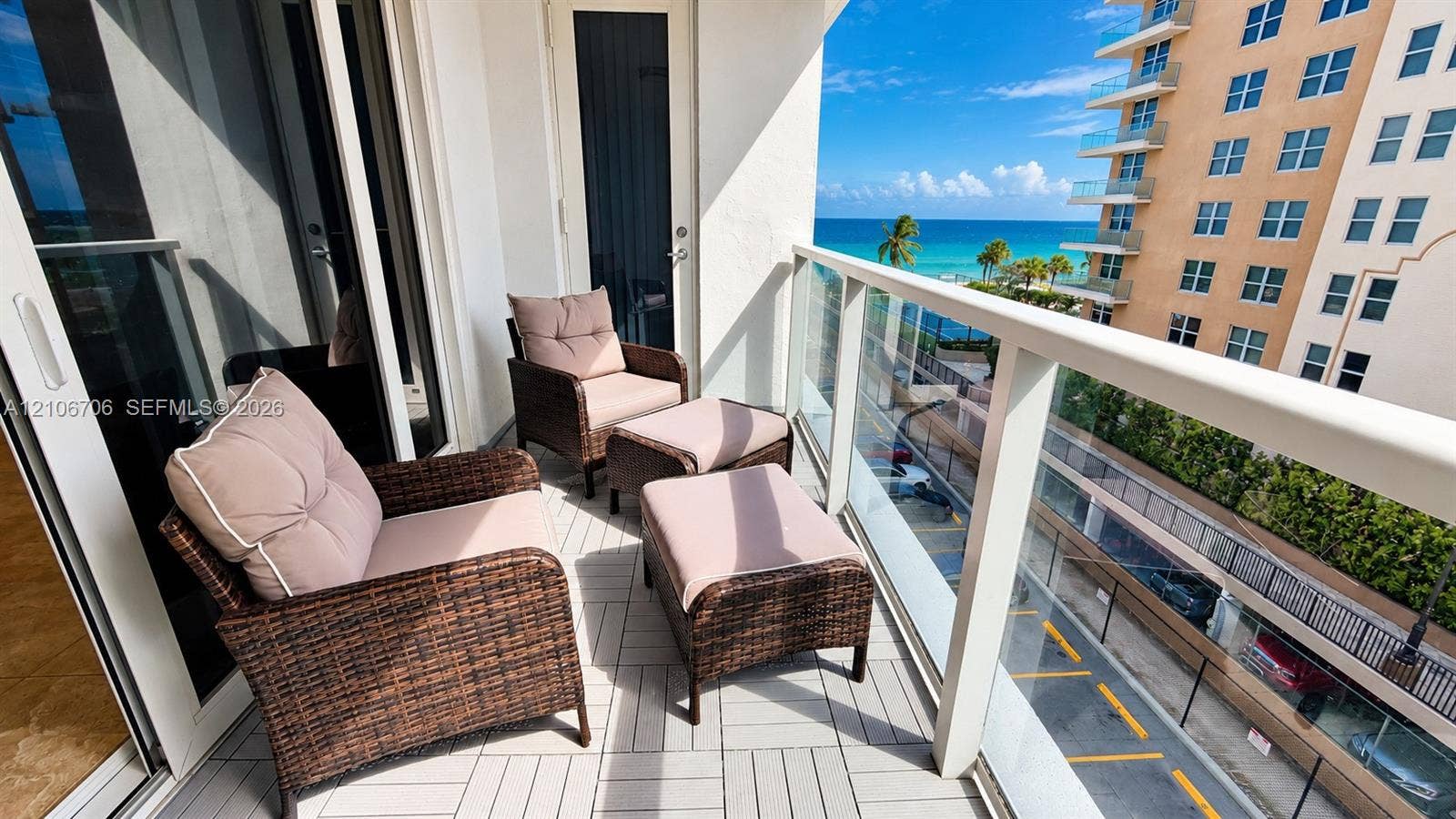 Private balcony featuring light-toned modular deck tiles, white metal railings with glass panel inserts, and direct access through large sliding glass doors