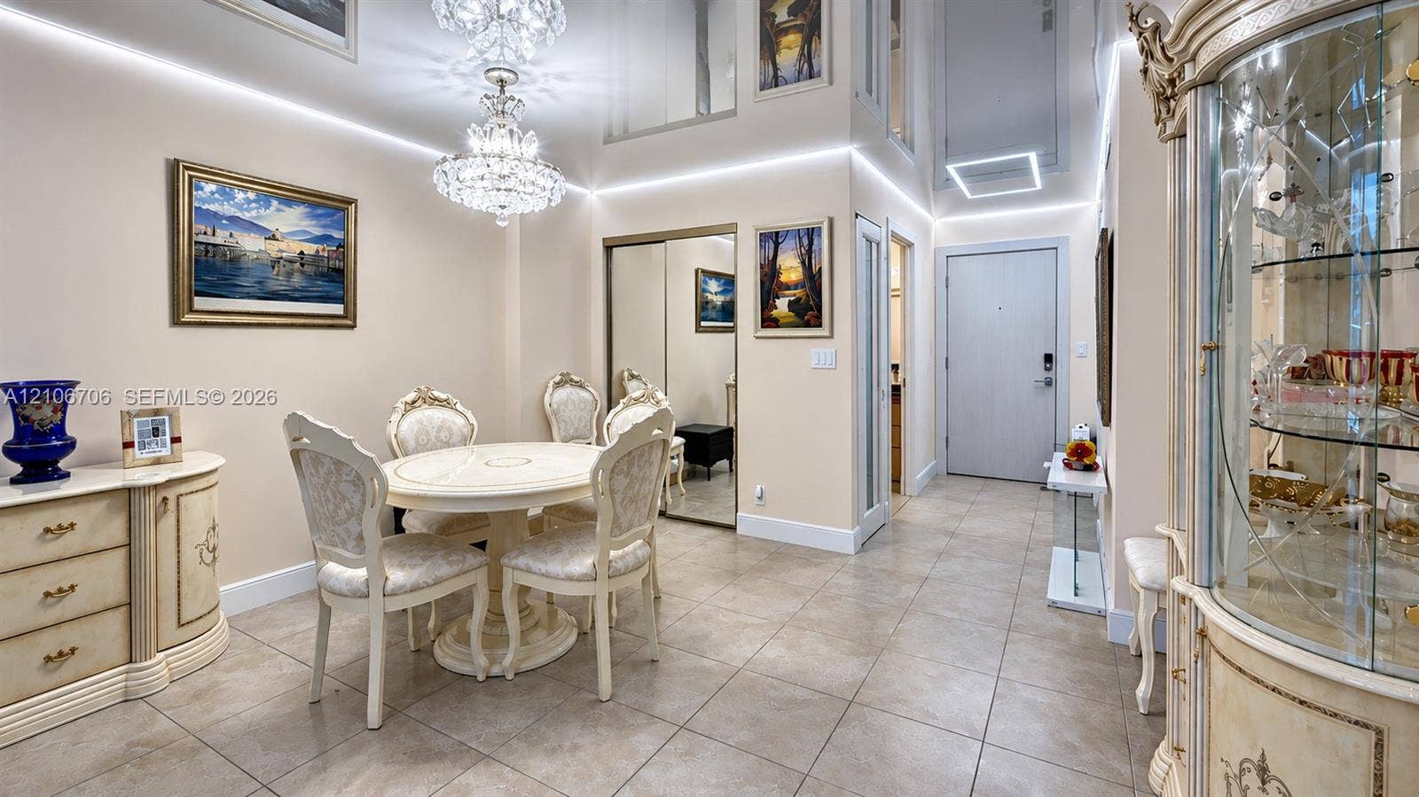 High-ceiling entryway featuring recessed linear LED perimeter lighting, a multi-tiered crystal chandelier, large-format tile flooring, and mirrored closet doors