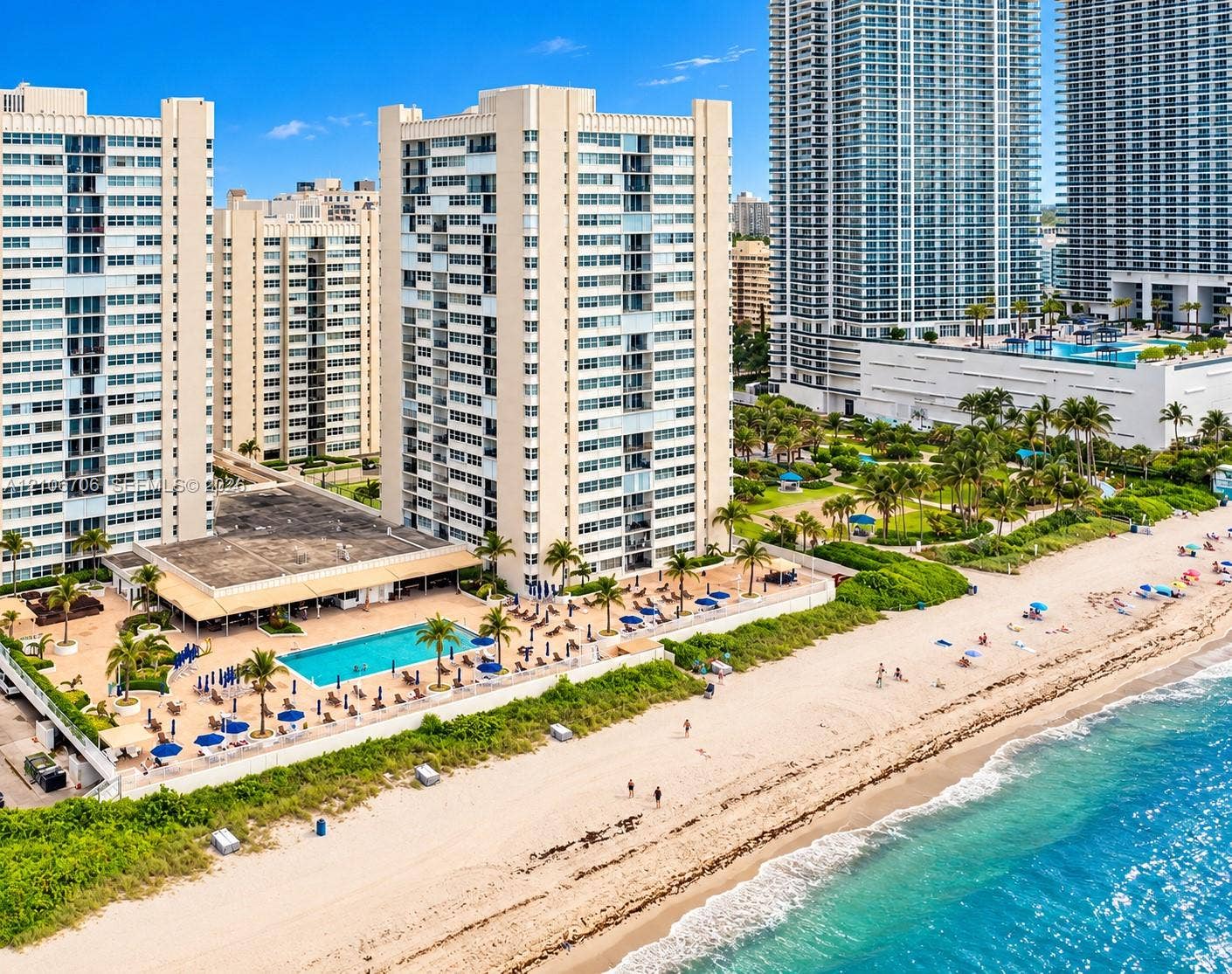 High-rise residential building featuring an outdoor swimming pool, paved sundeck, landscaped grounds, and direct beach access