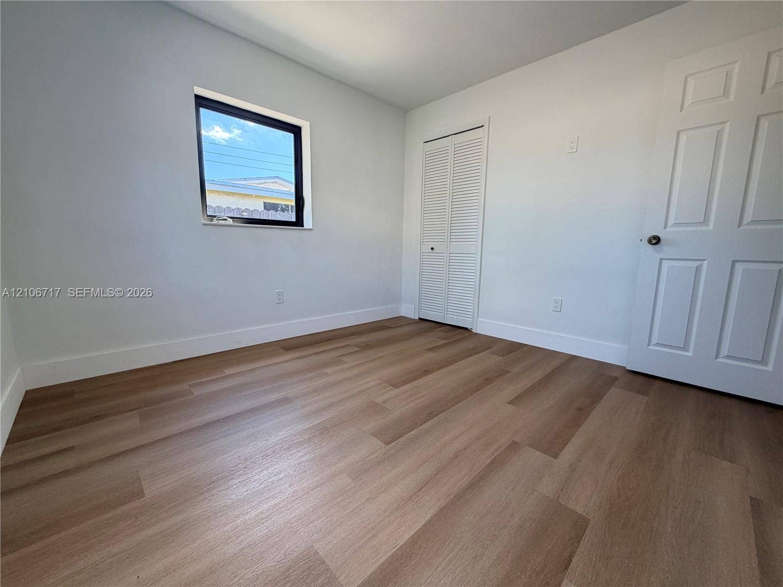 6811 Thomas Street, Hollywood, FL 33024 Wood-finish flooring, neutral wall tones, single-pane window, louvered-style closet doors, and a paneled interior door