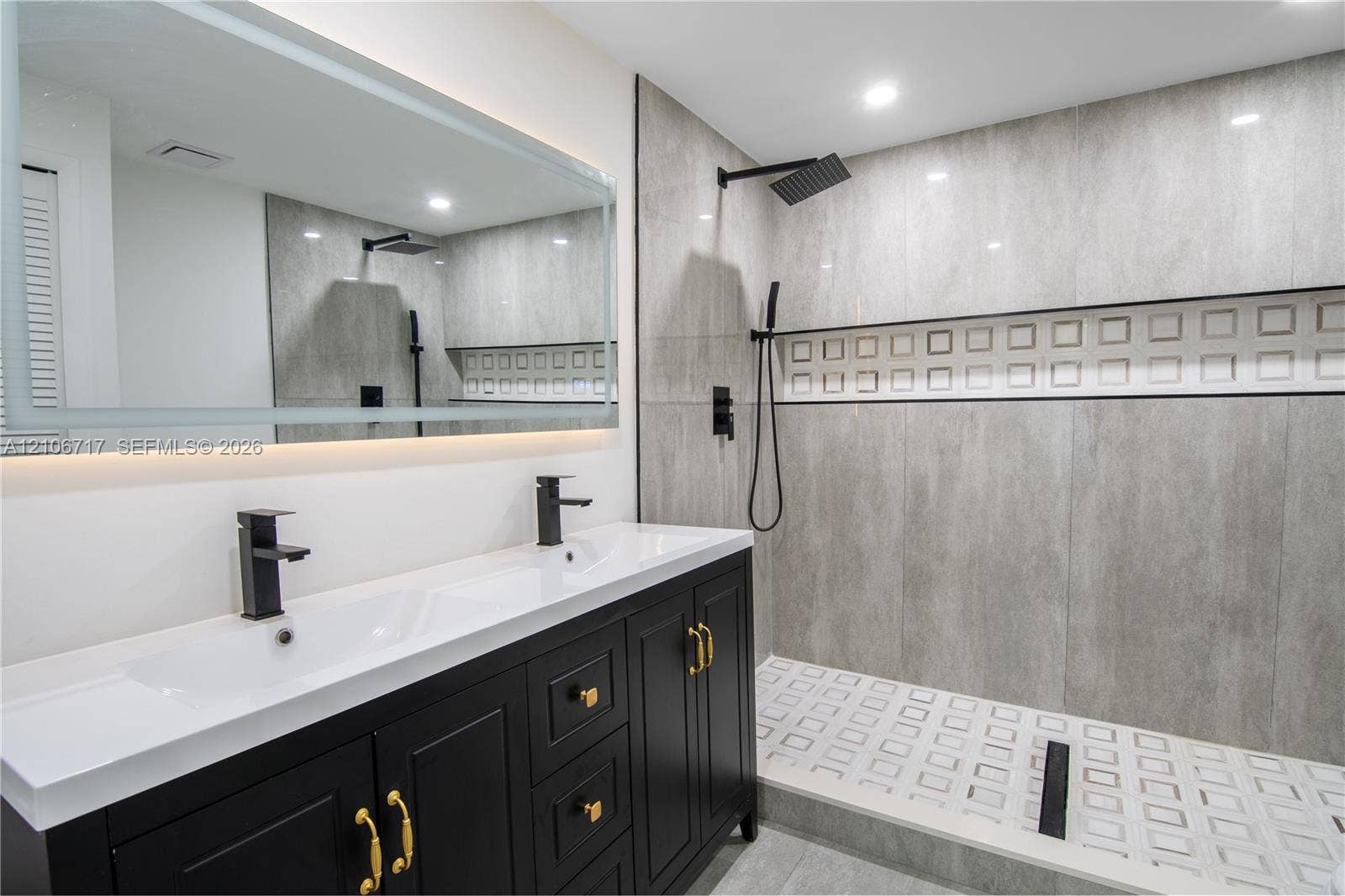 6811 Thomas Street, Hollywood, FL 33024 Black vanity with dual undermount sinks, large rectangular mirror with integrated lighting, and walk-in shower featuring matte black rainfall showerhead, textured tile accent wall, and patterned tile flooring