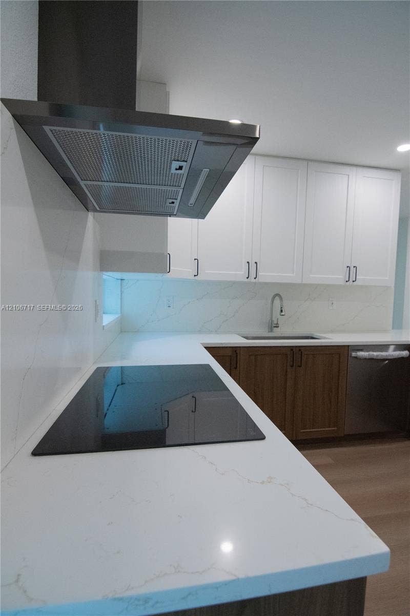 6811 Thomas Street, Hollywood, FL 33024 Kitchen featuring white stone-finish countertops with matching backsplash, white upper cabinetry, wood-finish lower cabinetry, a stainless steel chimney-style range hood, and a flat-surface cooktop