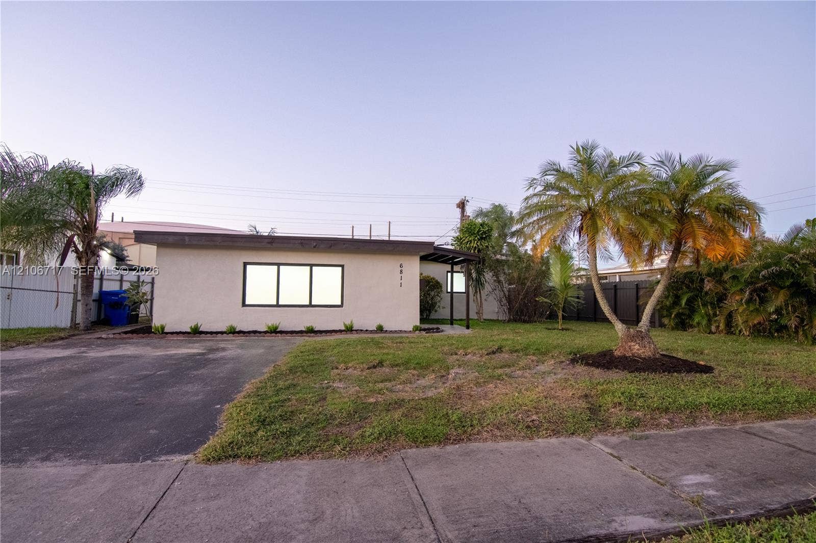 6811 Thomas Street, Hollywood, FL 33024 Single-story residence featuring a smooth stucco exterior, flat roofline, asphalt driveway, and manicured landscaping with established palm trees