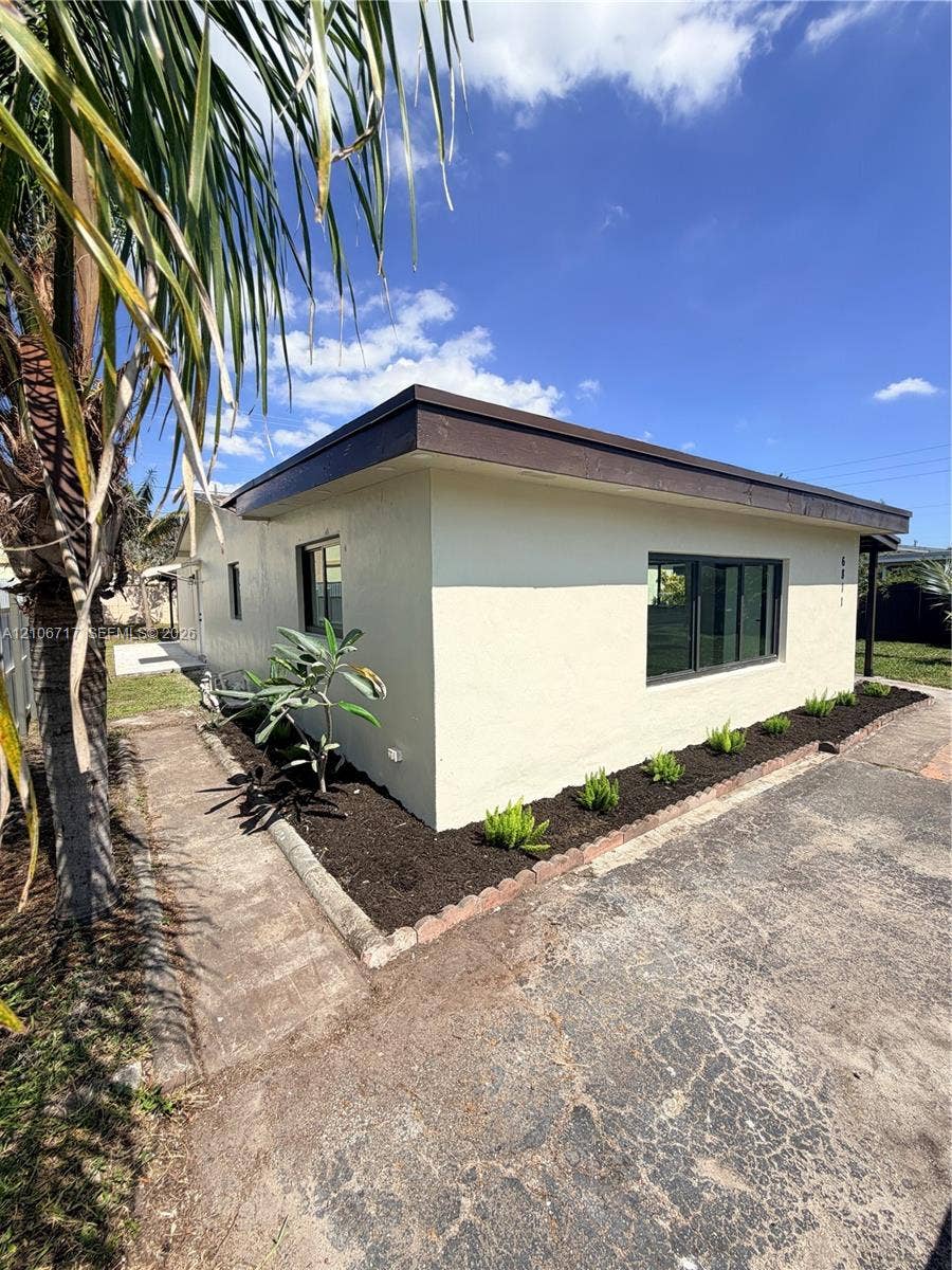 6811 Thomas Street, Hollywood, FL 33024 Exterior featuring a stucco facade, dark-toned trim, and modern dual-pane windows, complemented by a landscaped mulch bed and a concrete walkway