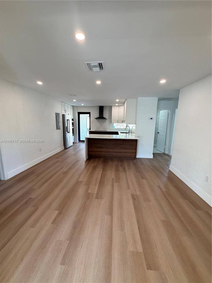 6811 Thomas Street, Hollywood, FL 33024 Open floor plan featuring wood-finish flooring, recessed lighting, white cabinetry, a kitchen island with a wood-tone base, and a wall-mounted chimney-style range hood