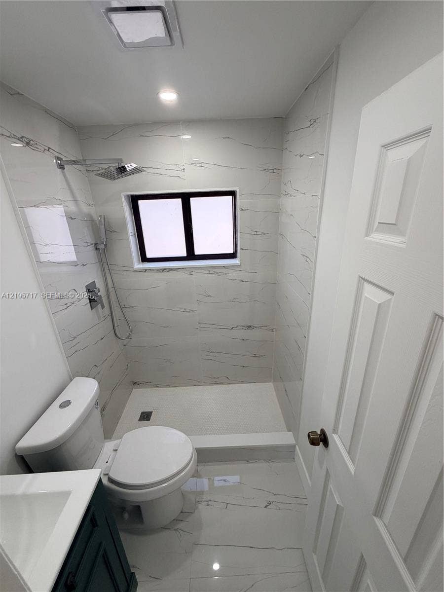 6811 Thomas Street, Hollywood, FL 33024 Full-bathroom featuring floor-to-ceiling large-format tile, a walk-in shower with a rainfall showerhead, a modern vanity, and a dual-flush toilet