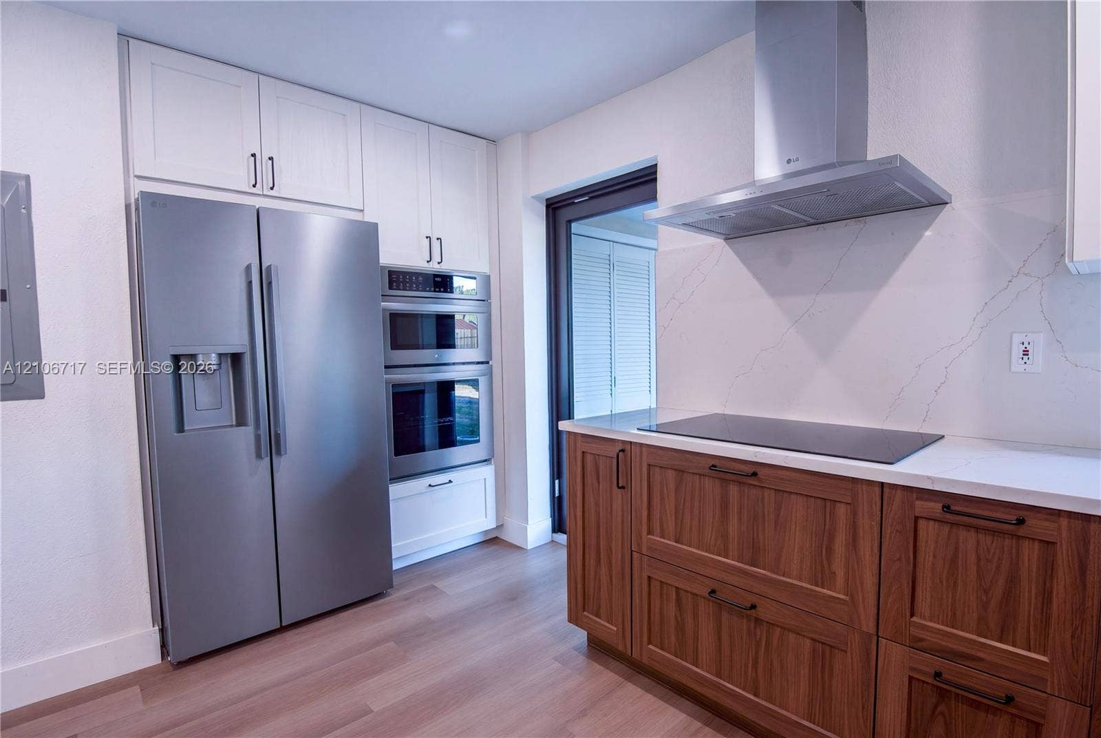 6811 Thomas Street, Hollywood, FL 33024 Kitchen featuring wood-finish lower cabinetry, white upper cabinetry, stainless steel double wall ovens, stainless steel refrigerator, and quartz countertops with integrated backsplash