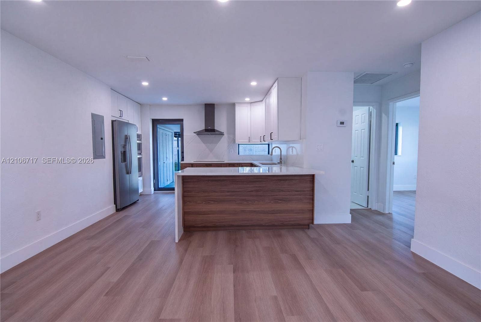 6811 Thomas Street, Hollywood, FL 33024 Kitchen featuring white upper cabinetry, wood-finish lower cabinetry, stone-surface countertops, stainless steel range hood, and wood-finish flooring