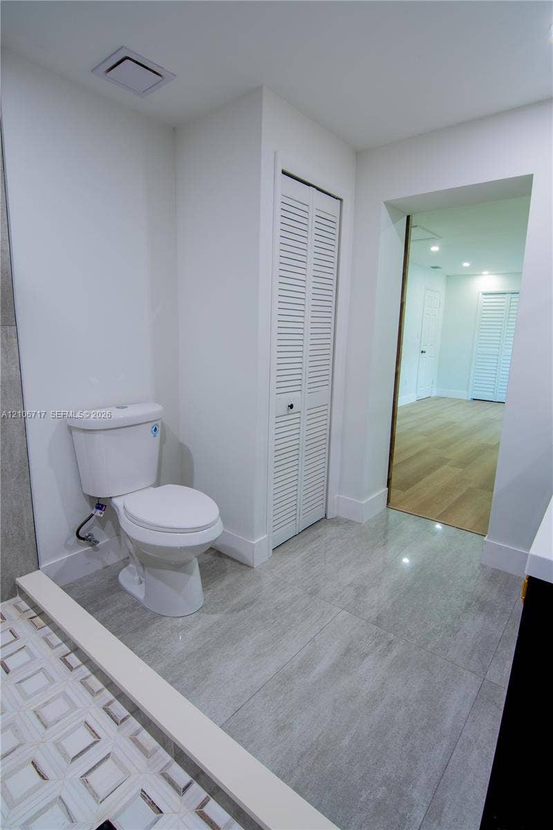 6811 Thomas Street, Hollywood, FL 33024 Bathroom featuring large-format ceramic tile flooring, a white porcelain toilet, and a closet with white louvered doors